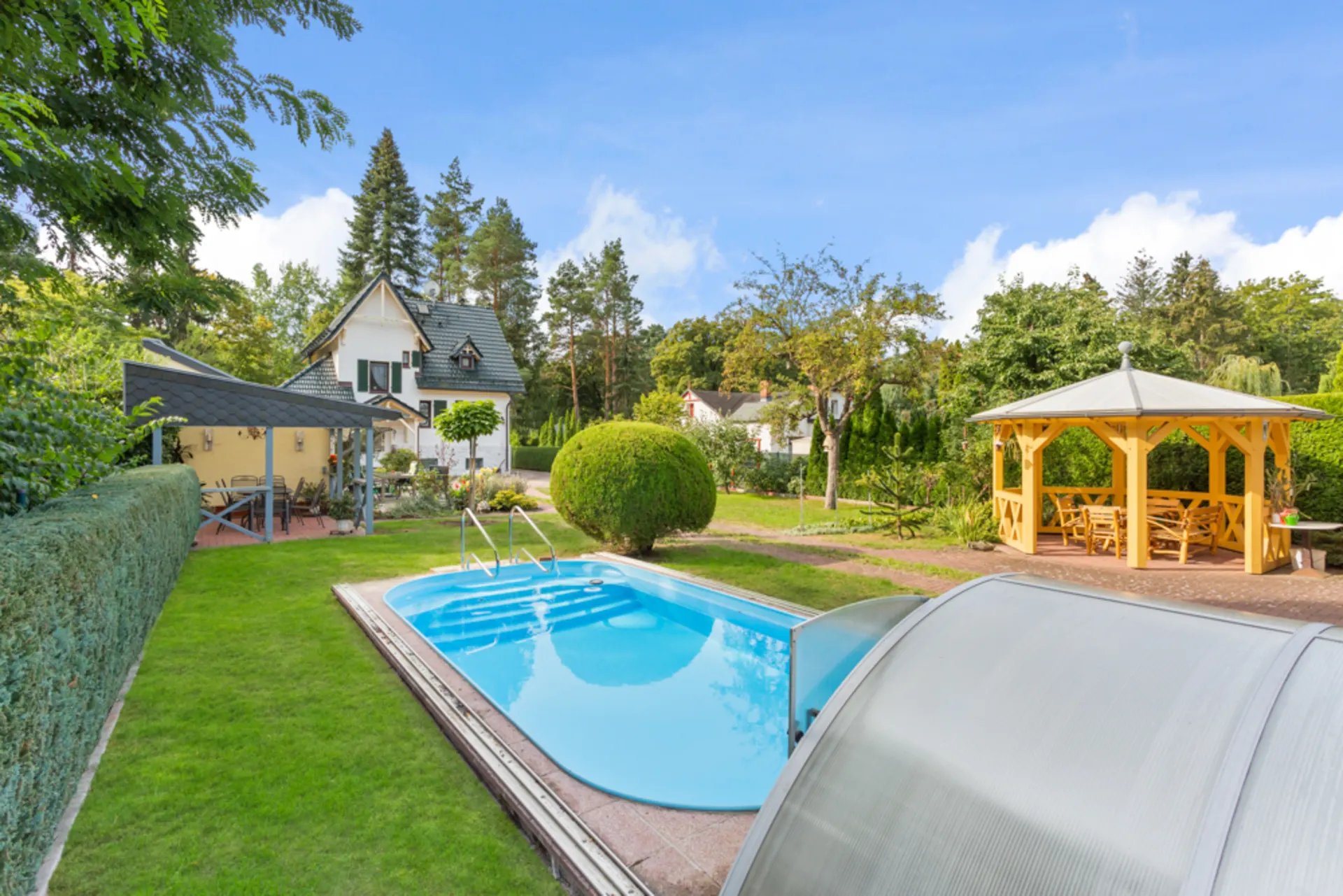 Garten mit Swimmingpool, Pavillon und Haus im Hintergrund an einem sonnigen Tag.