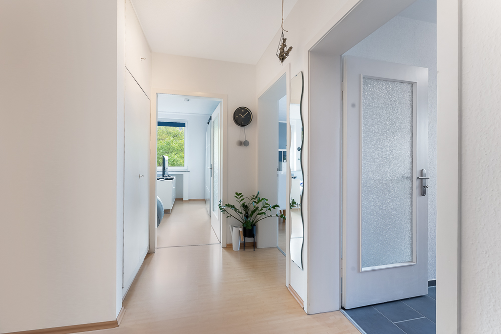 Heller Flur mit Holzboden, Spiegel, Uhr an der Wand und mehreren Türen.