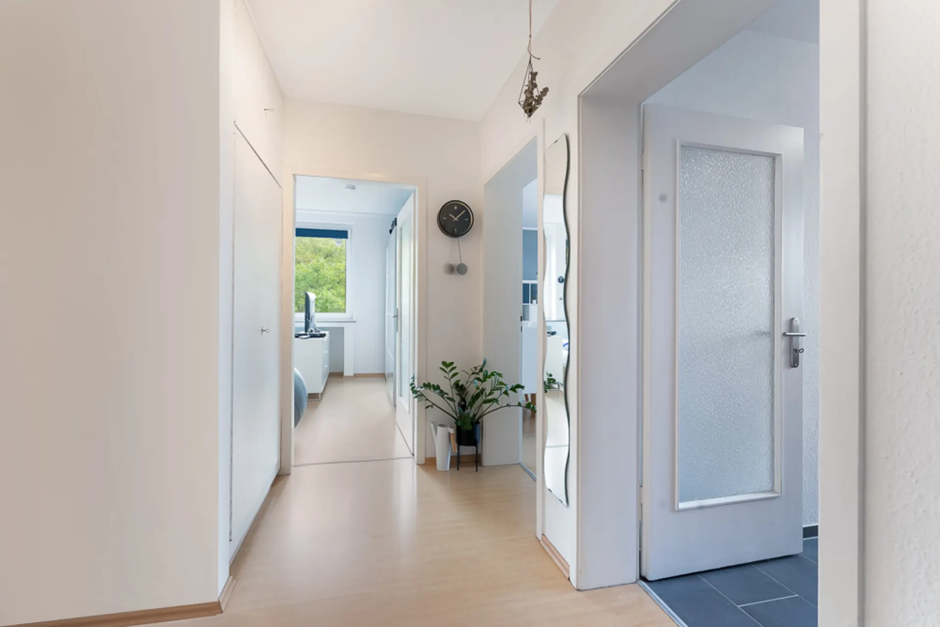Heller Flur mit Holzboden, Spiegel, Uhr an der Wand und mehreren Türen.