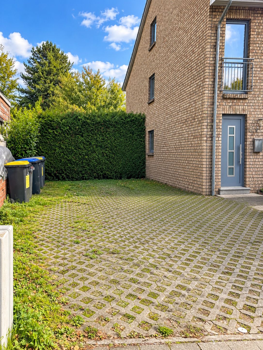 Gepflasterter Hof mit Mülltonnen neben einem Wohnhaus und Hecke im Hintergrund.