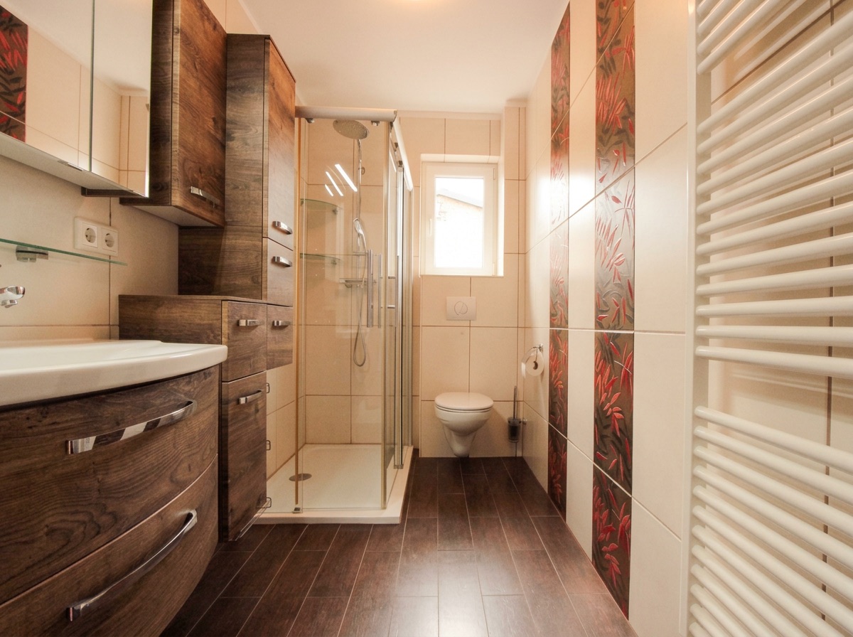 Modernes Badezimmer mit Holzschränken, Glasdusche, WC und Handtuchheizkörper.