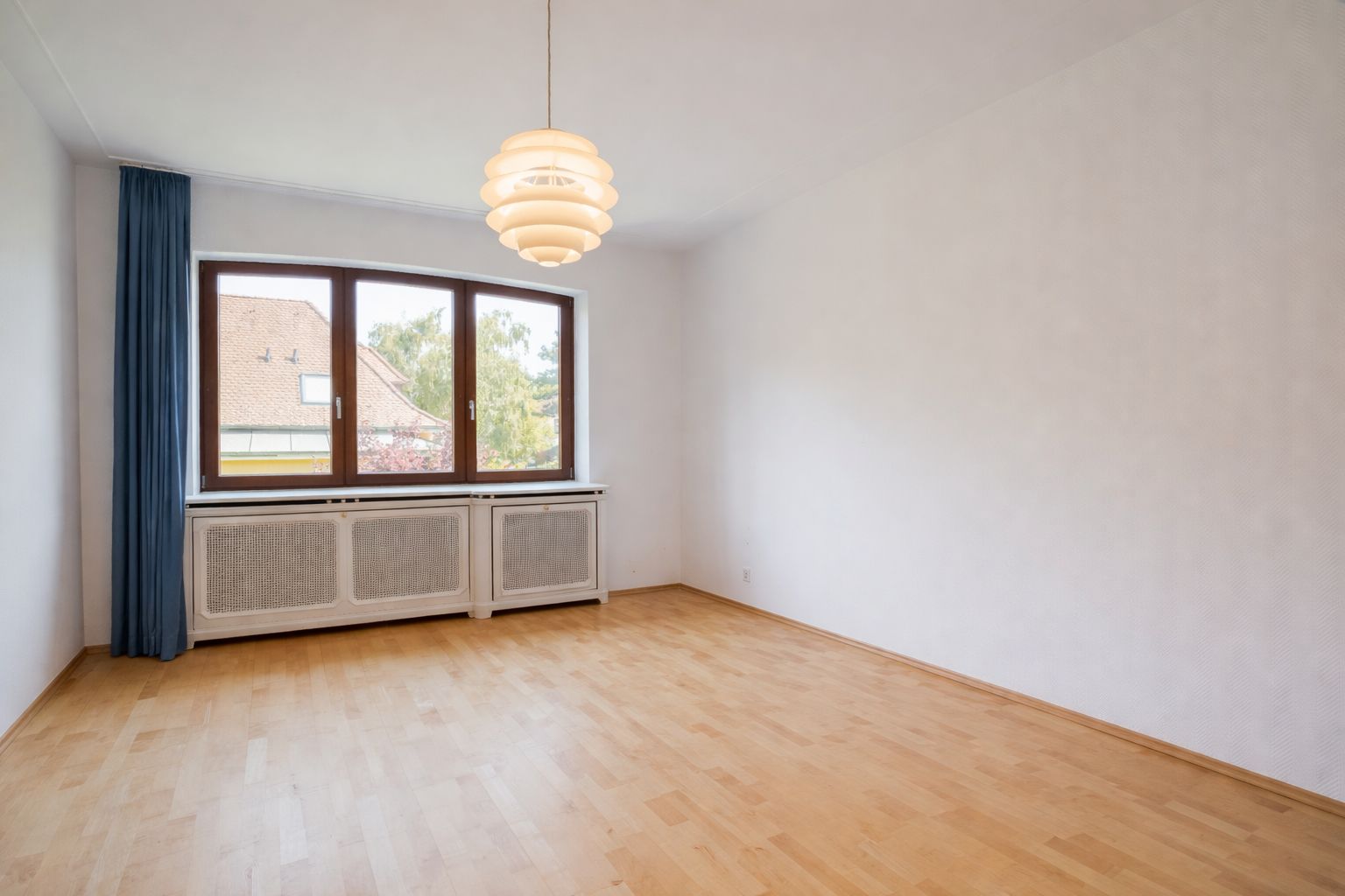 Leerer Raum mit Holzboden, großem Fenster und Deckenleuchte.