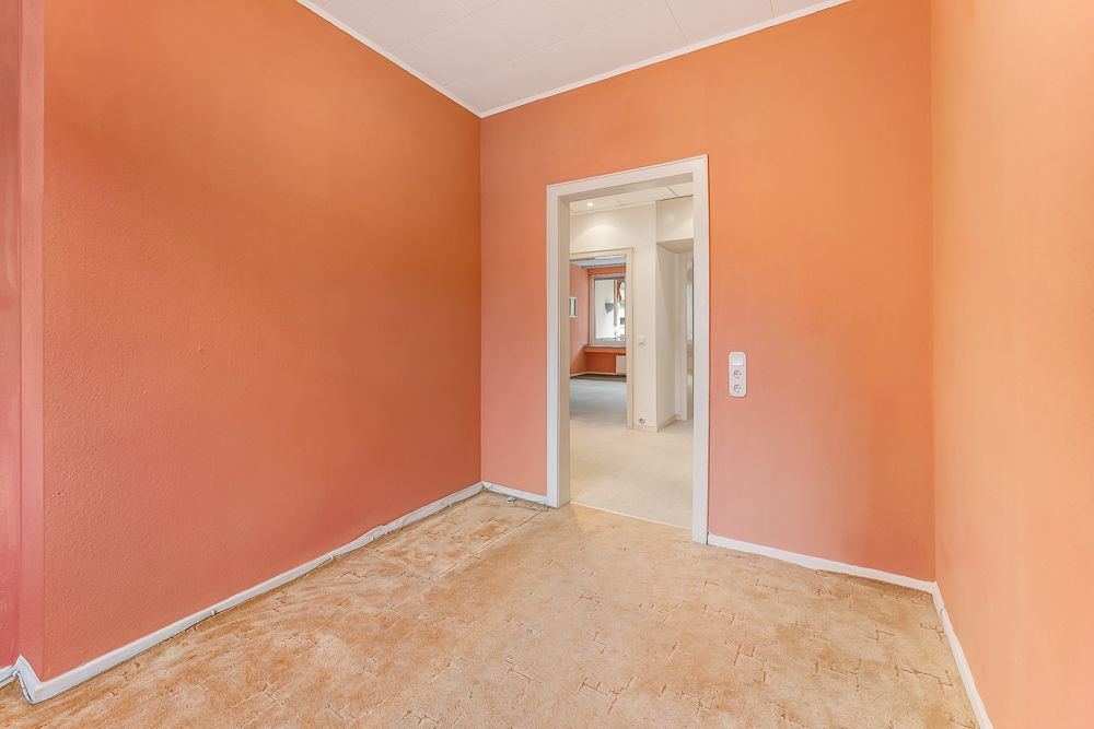 Leerer Raum mit orangenen Wänden und hellem, unfertigem Boden, Blick durch Tür in weiteren Raum.