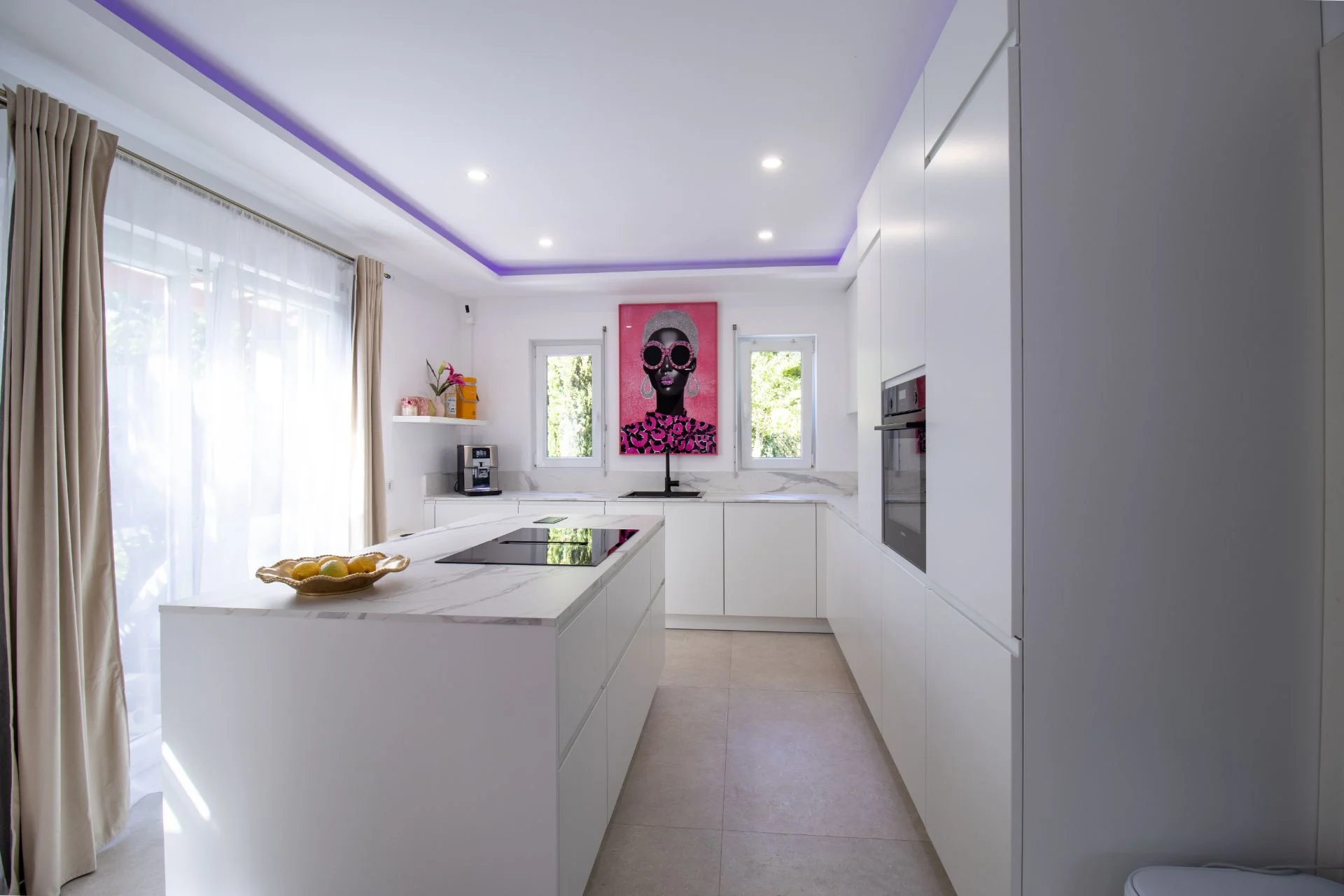 Moderne weiße Küche mit Kochinsel, großem Fenster und einem bunten Bild an der Wand.
