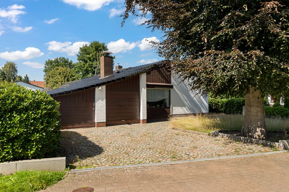 Einfamilienhaus mit geneigtem Dach, großer Einfahrt und Baum im Vorgarten.