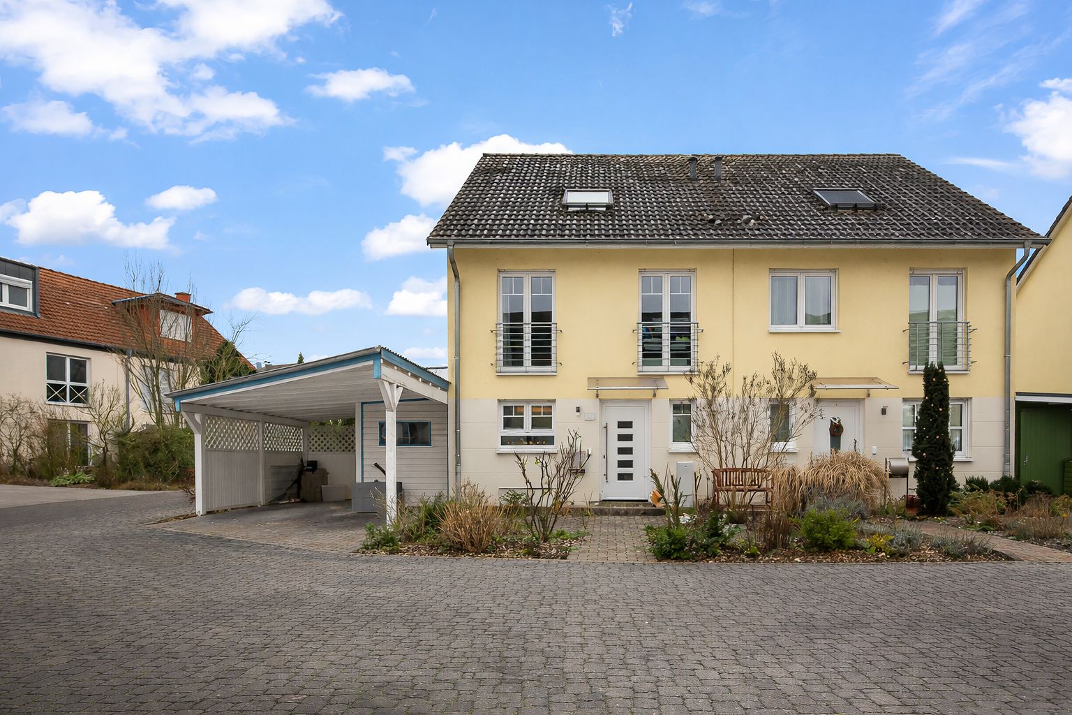 Doppelhaushälfte mit gelber Fassade, Carport und kleinem Garten vorne.