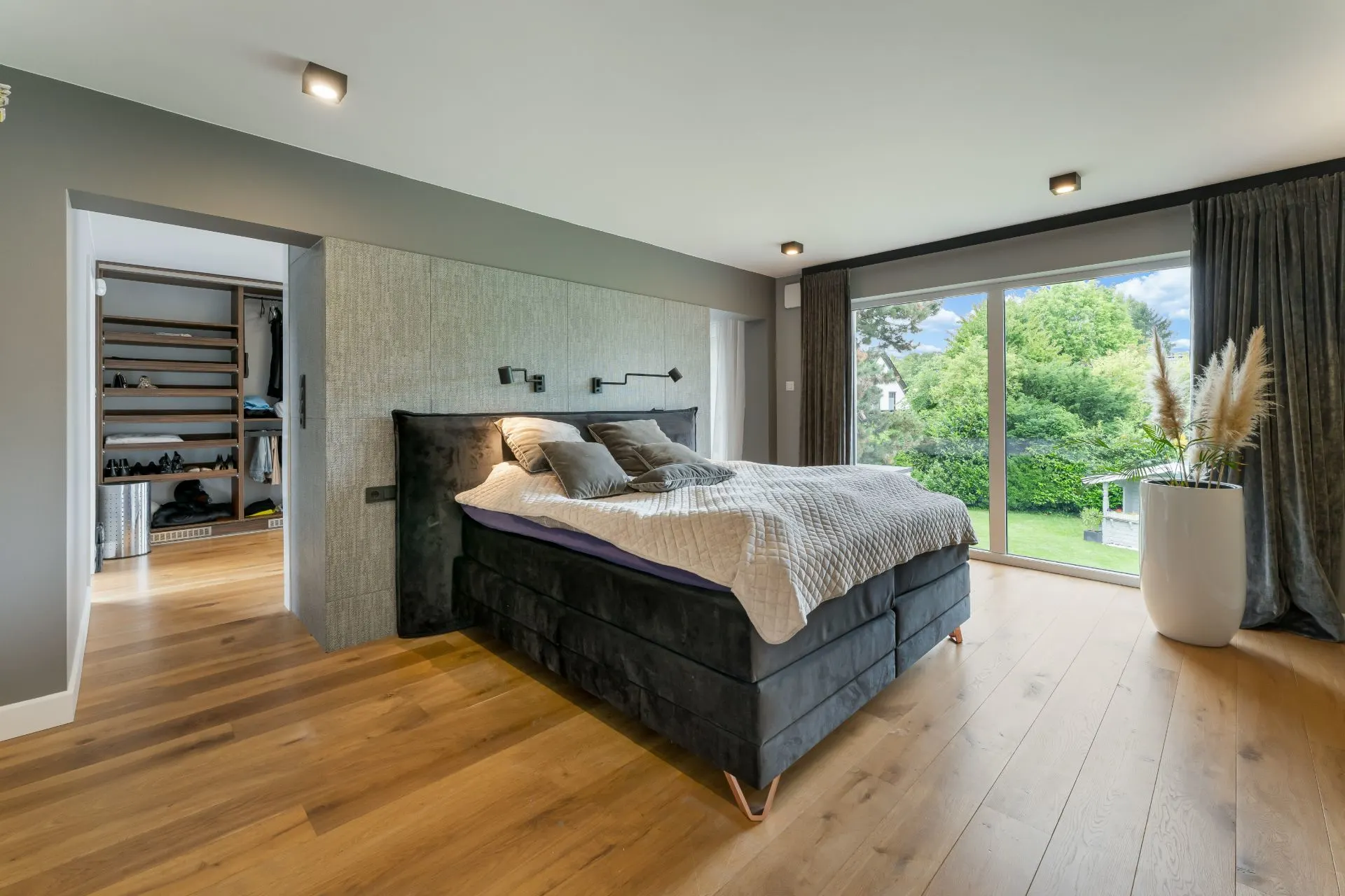 Modernes Schlafzimmer mit Doppelbett, Holzboden und großem Fenster mit Blick auf Garten.