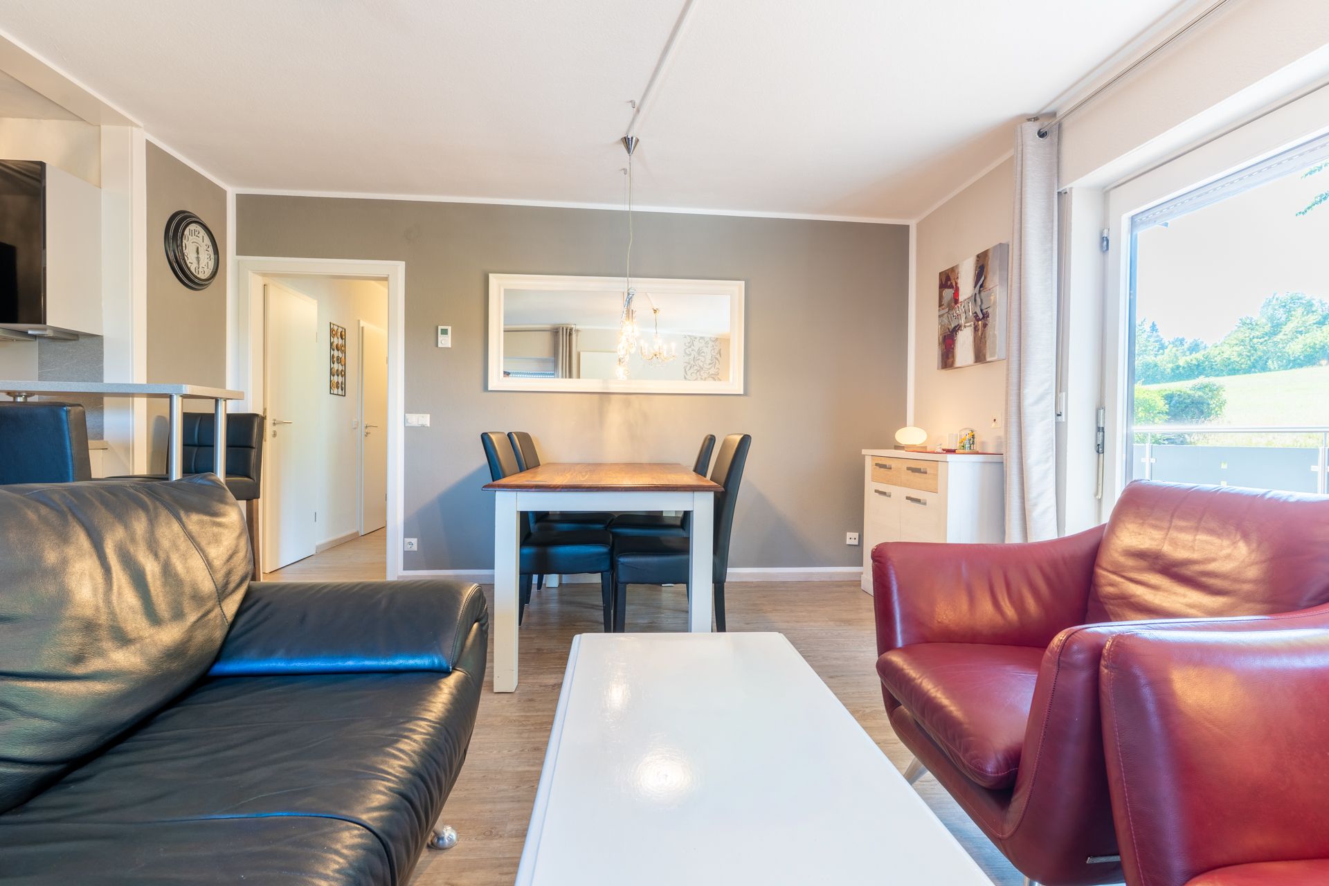 Wohnzimmer mit schwarzem Sofa, rotem Sessel, Esstisch und großem Fenster.