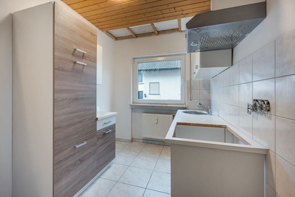 Leere, moderne Küche mit Fliesenboden, Holzdecke, Fenster und Einbauschränken.