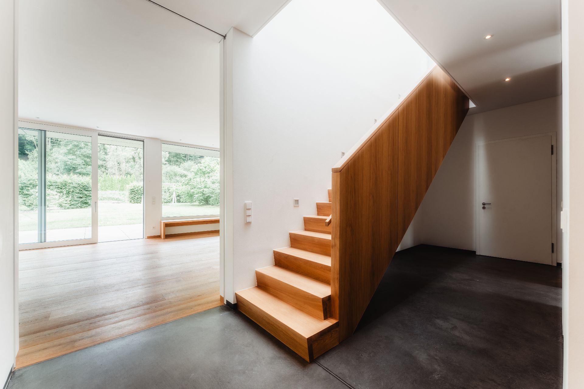 Helle Diele mit Holztreppe, großem Fenster und Blick ins Grüne.