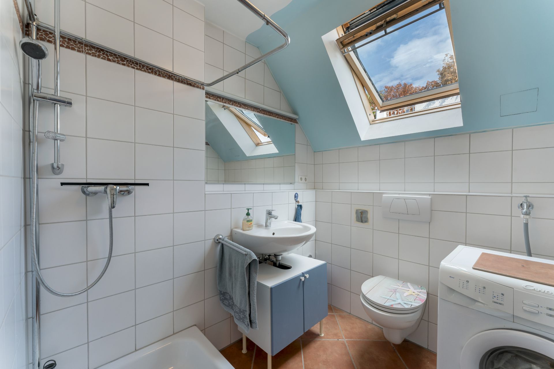 Modernes Badezimmer mit Dachfenster, Dusche, Waschbecken, Toilette und Waschmaschine.