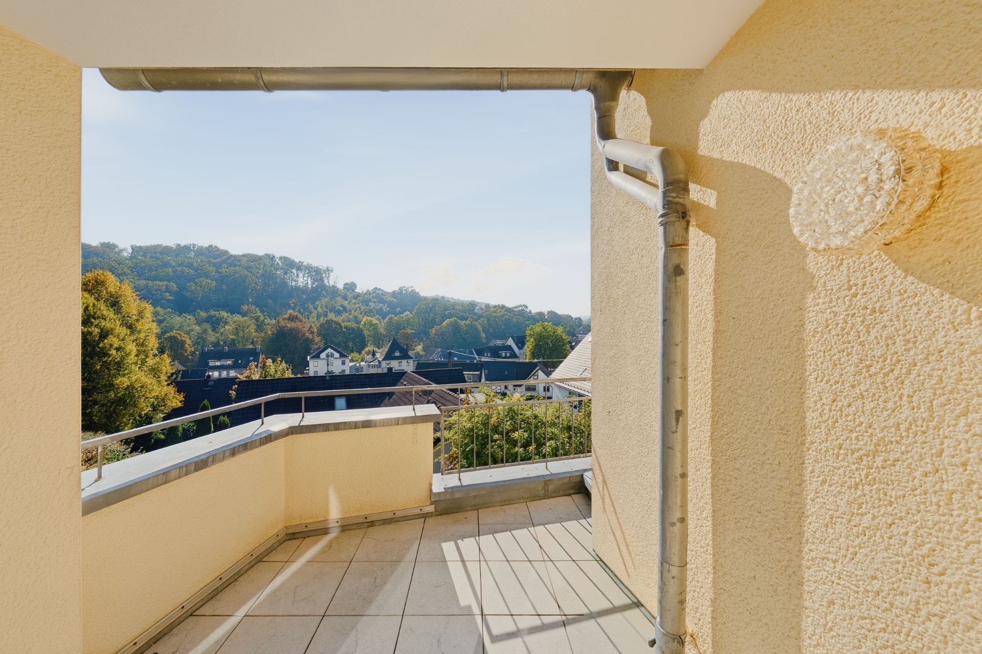 Balkon mit Geländer und Blick auf Bäume und Dächer in einer Wohngegend.