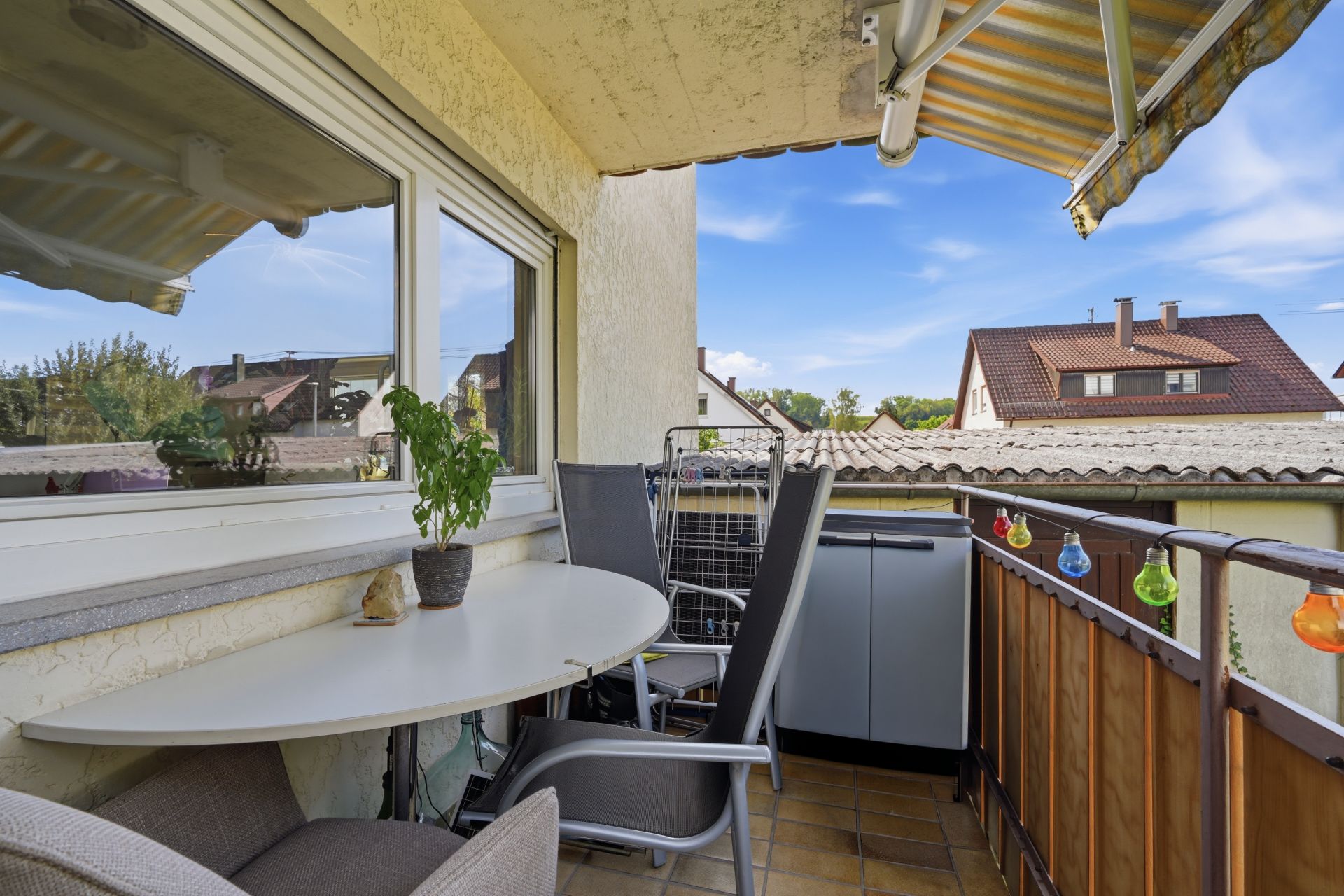 Kleiner Balkon mit Tisch, Stühlen, Pflanze und Lichterkette, Blick auf Nachbarhäuser.