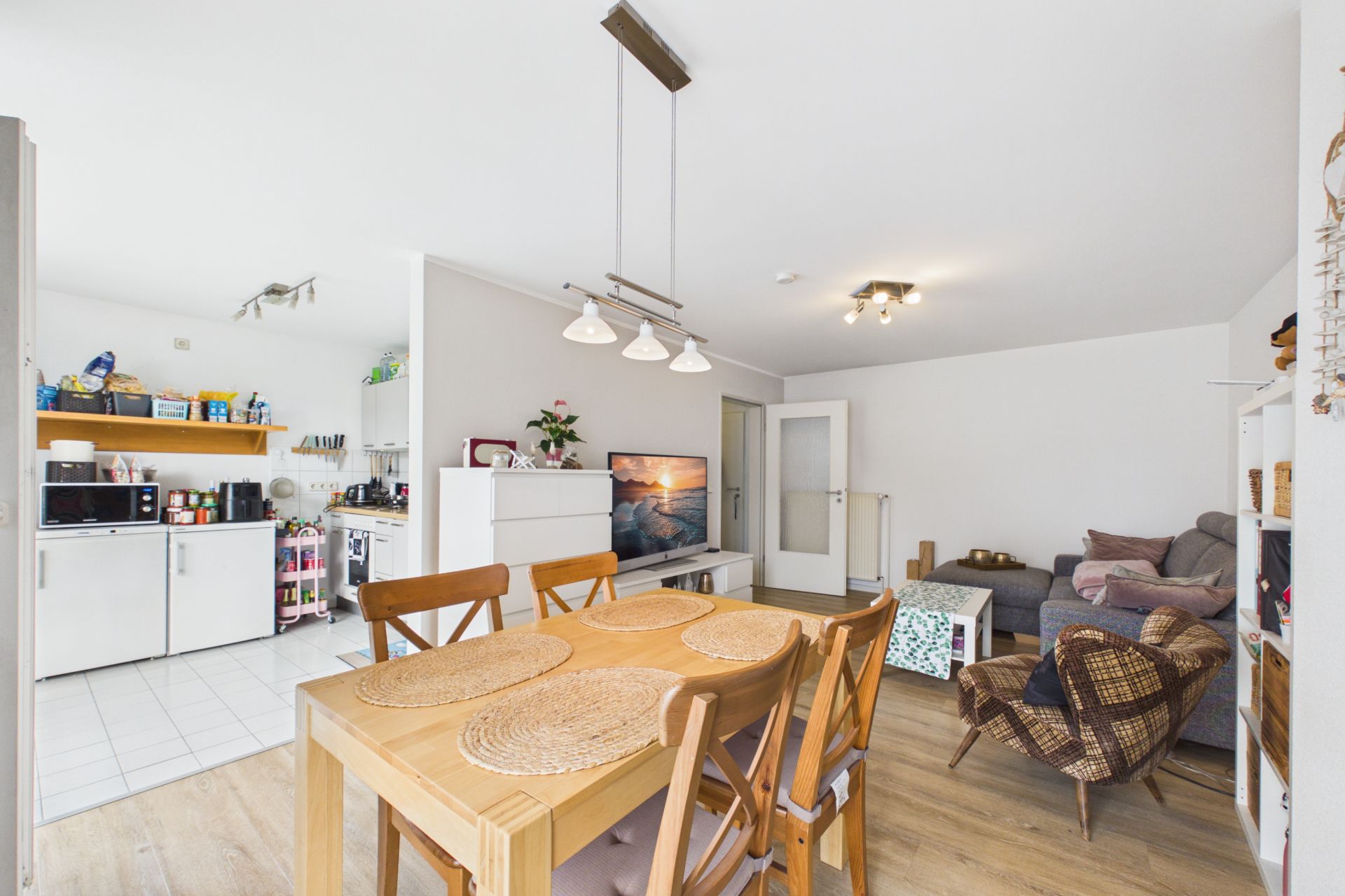 Wohnzimmer mit Essbereich, Holztisch, Stühlen, Sofa und offener Küche im Hintergrund.