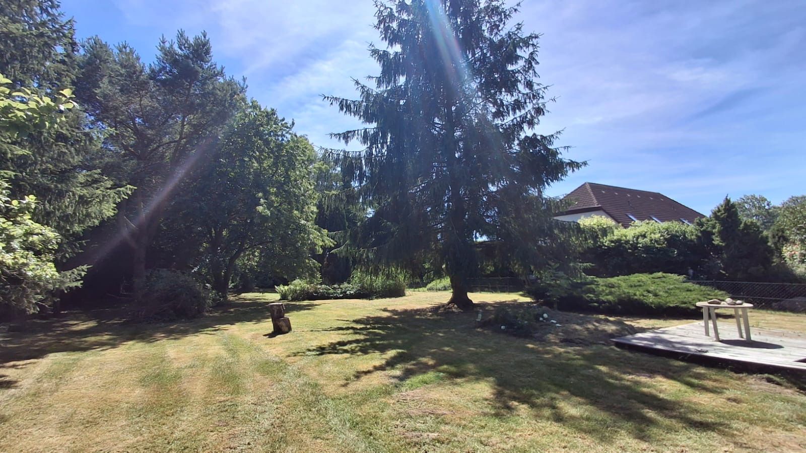 Großer Garten mit Rasen, Bäumen und einer Holzterrasse bei Tageslicht.