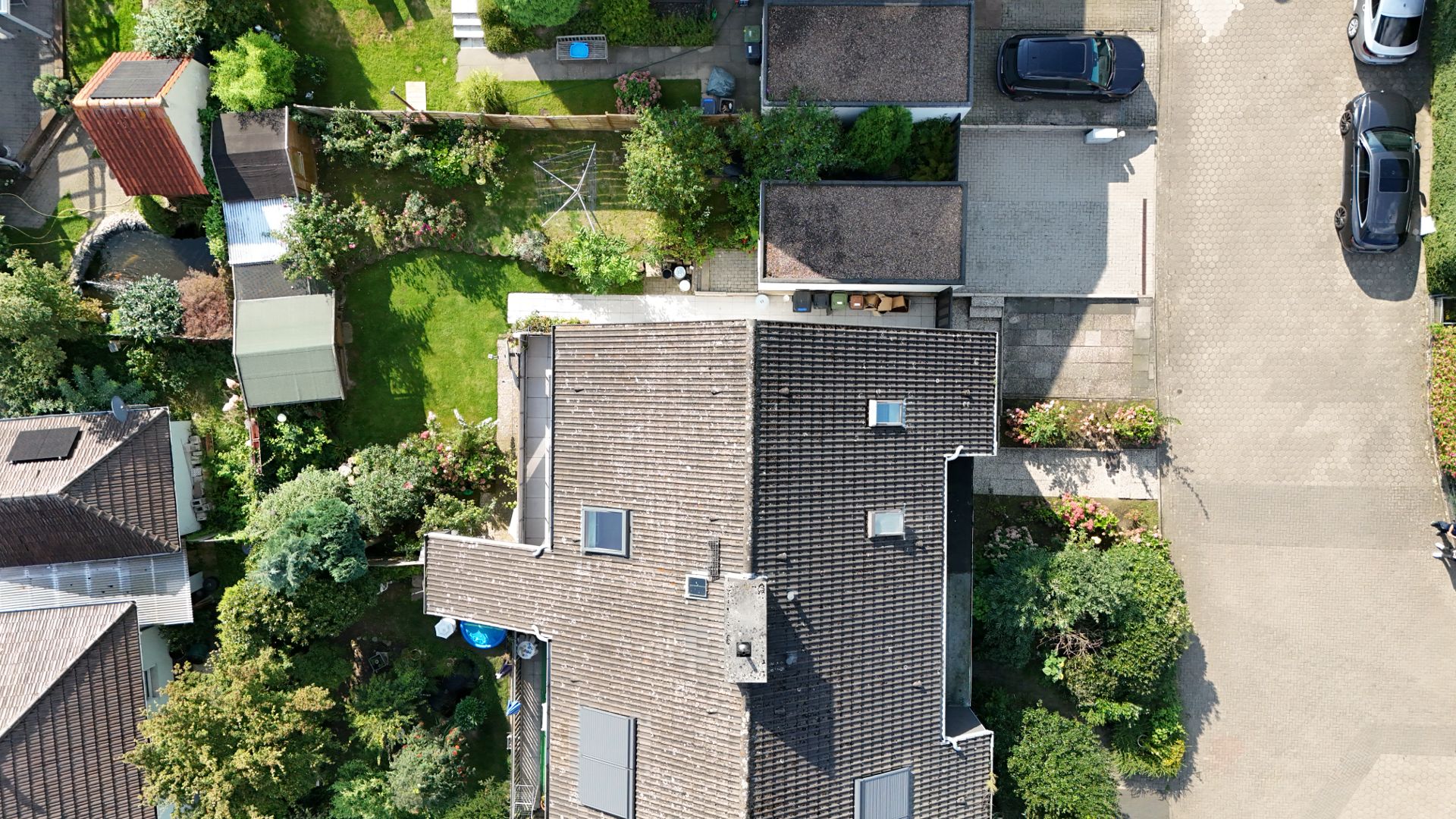 Luftaufnahme eines Wohnhauses mit Garten, Auffahrt und geparkten Autos.