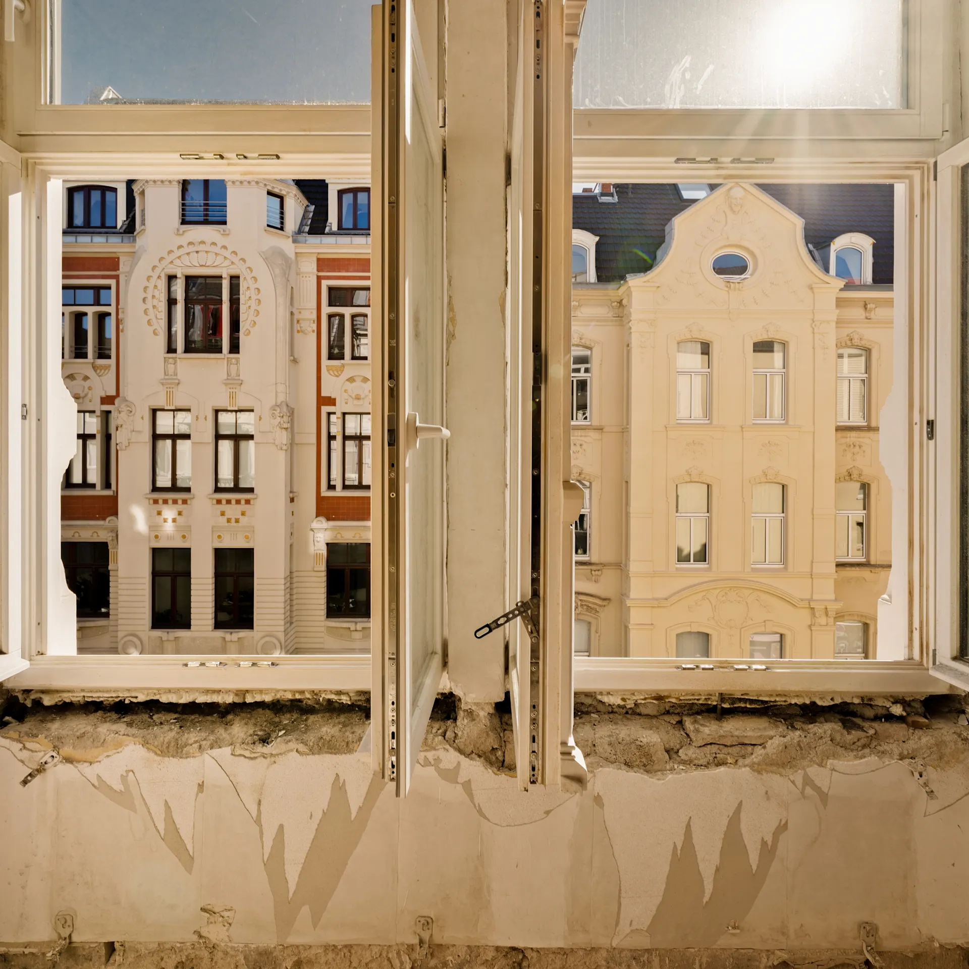 Blick aus einem renovierungsbedürftigen Raum durch offene Fenster auf Altbaufassaden.