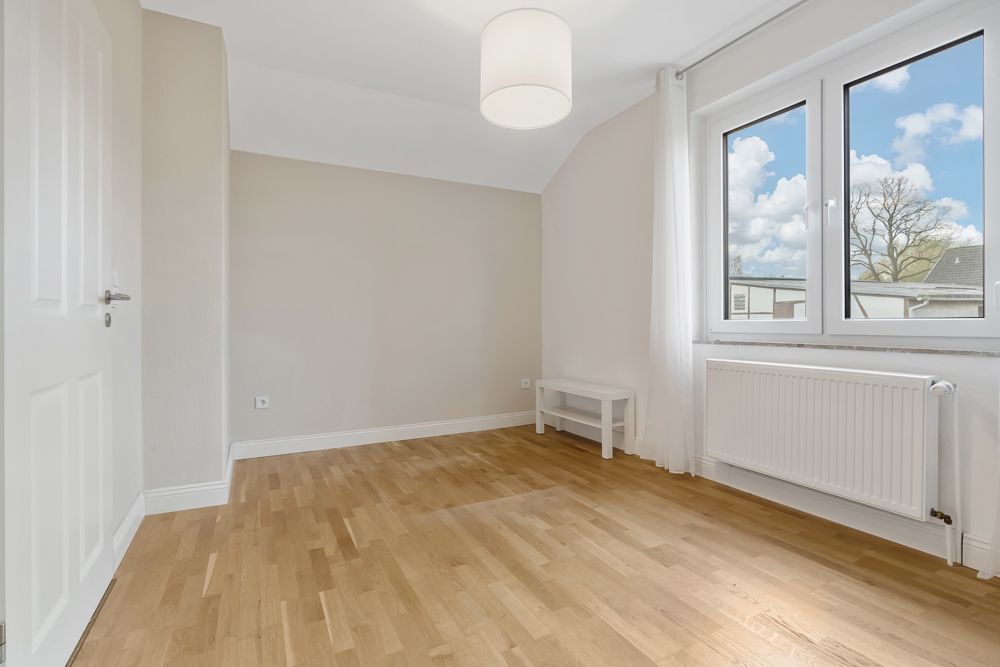 Heller, leerer Raum mit Holzfußboden, großem Fenster, weißem Tisch und Heizung.