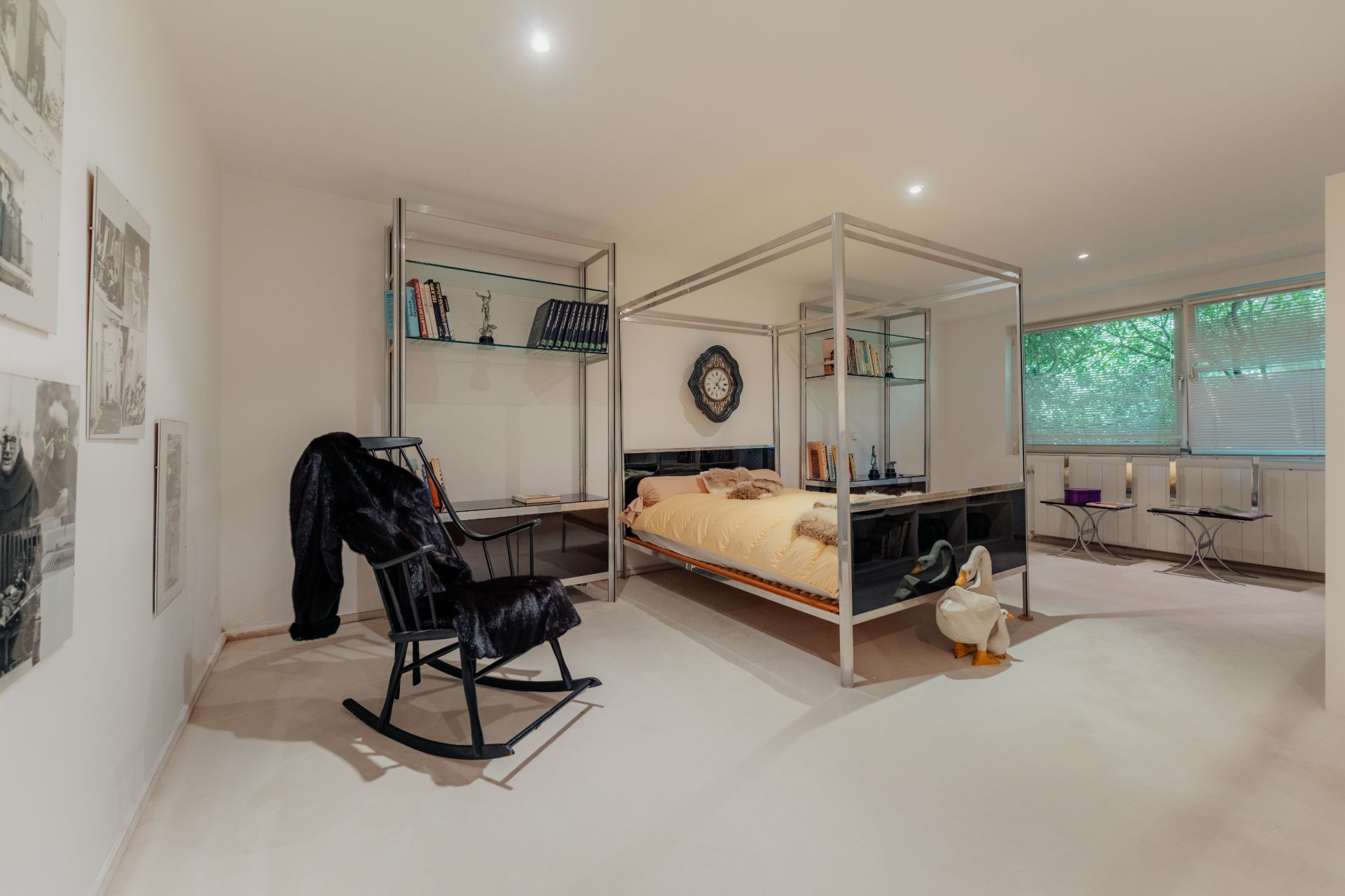 Helles Schlafzimmer mit Himmelbett, Schaukelstuhl und großen Fenstern mit Blick ins Grüne.