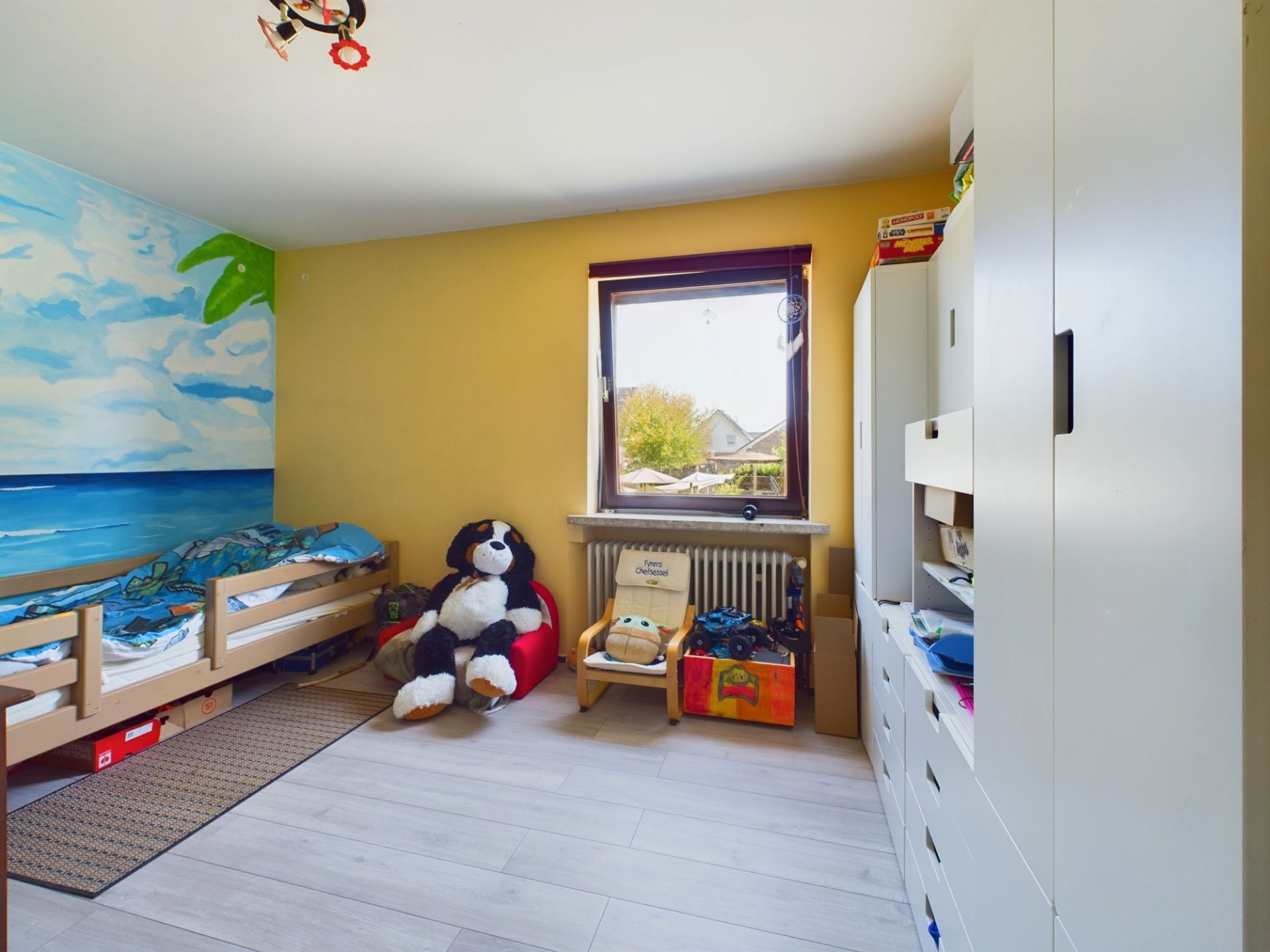 Kinderzimmer mit Bett, großem Stoffhund, Schrankwand und bemalter Wand mit Meeresmotiv.