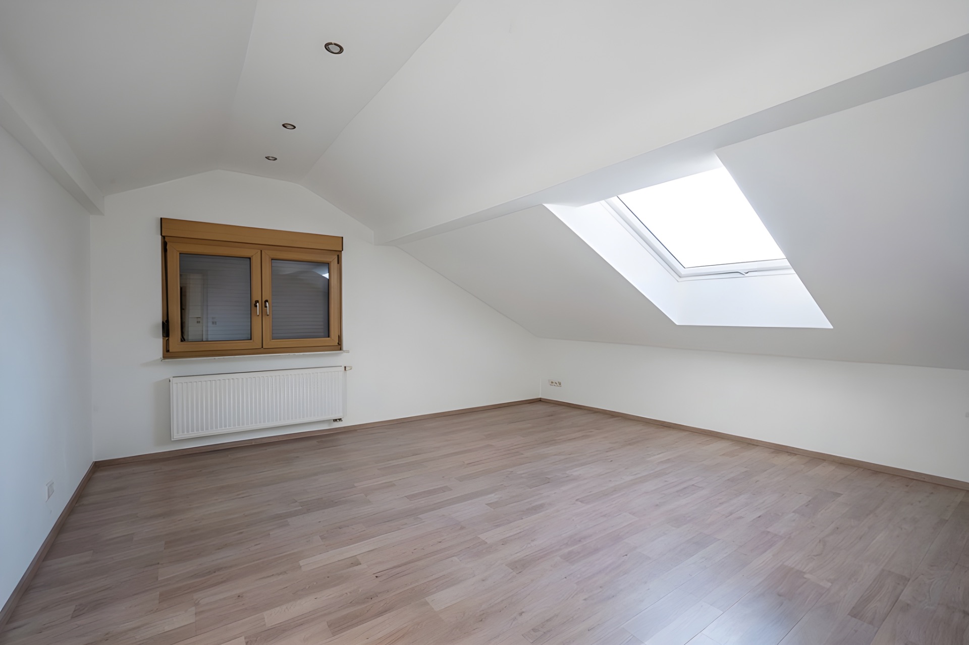 Leerer Dachgeschossraum mit Holzfenster, Dachfenster und Parkettboden.