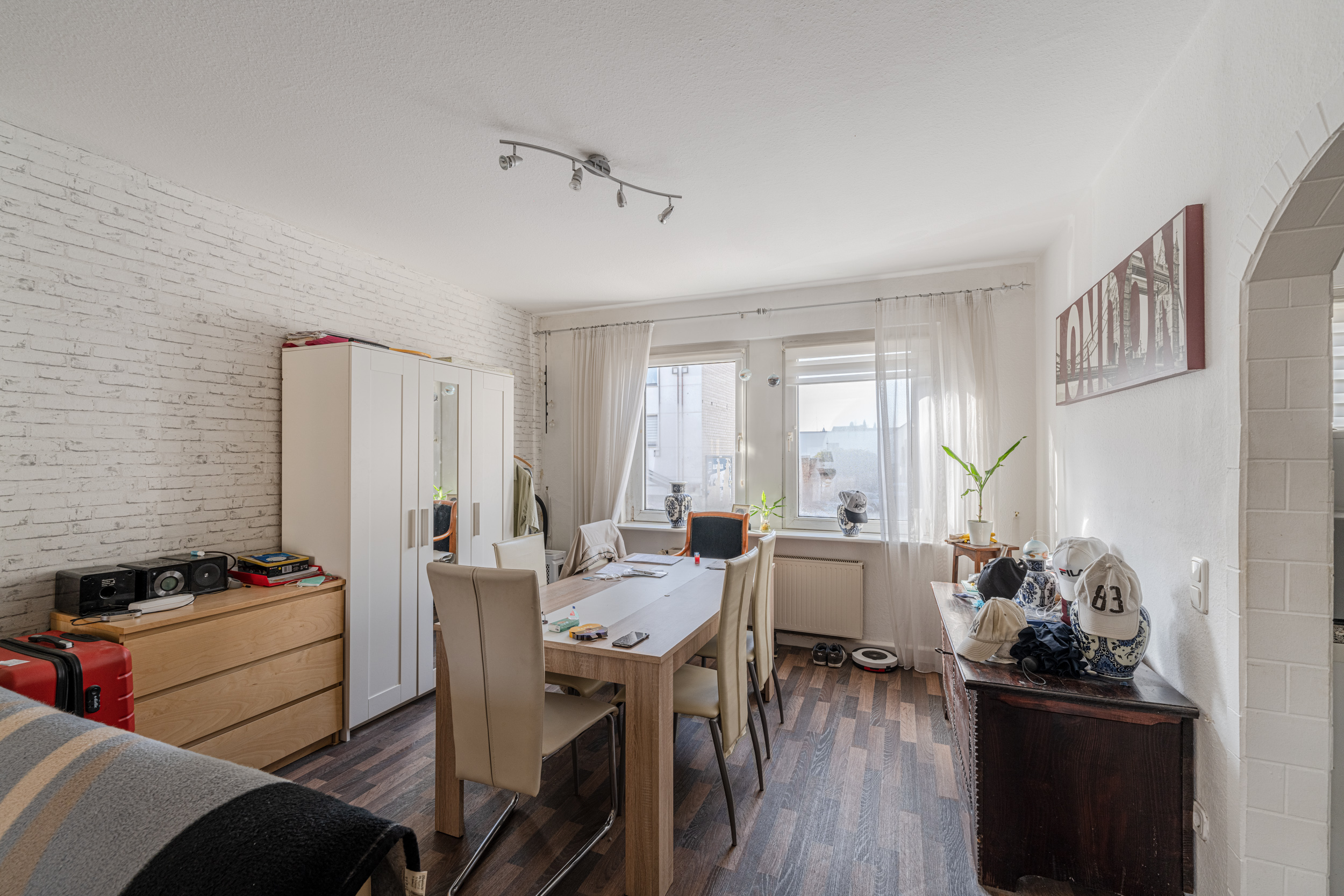 Helles Esszimmer mit Holztisch, sechs Stühlen, Schrank und zwei Fenstern mit Vorhängen.