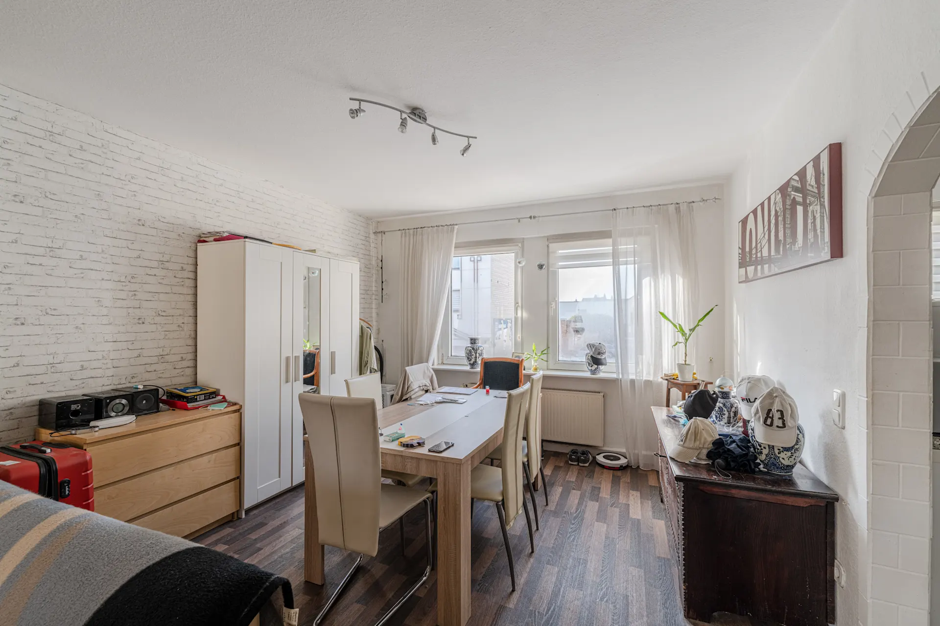 Helles Esszimmer mit Holztisch, sechs Stühlen, Schrank und zwei Fenstern mit Vorhängen.