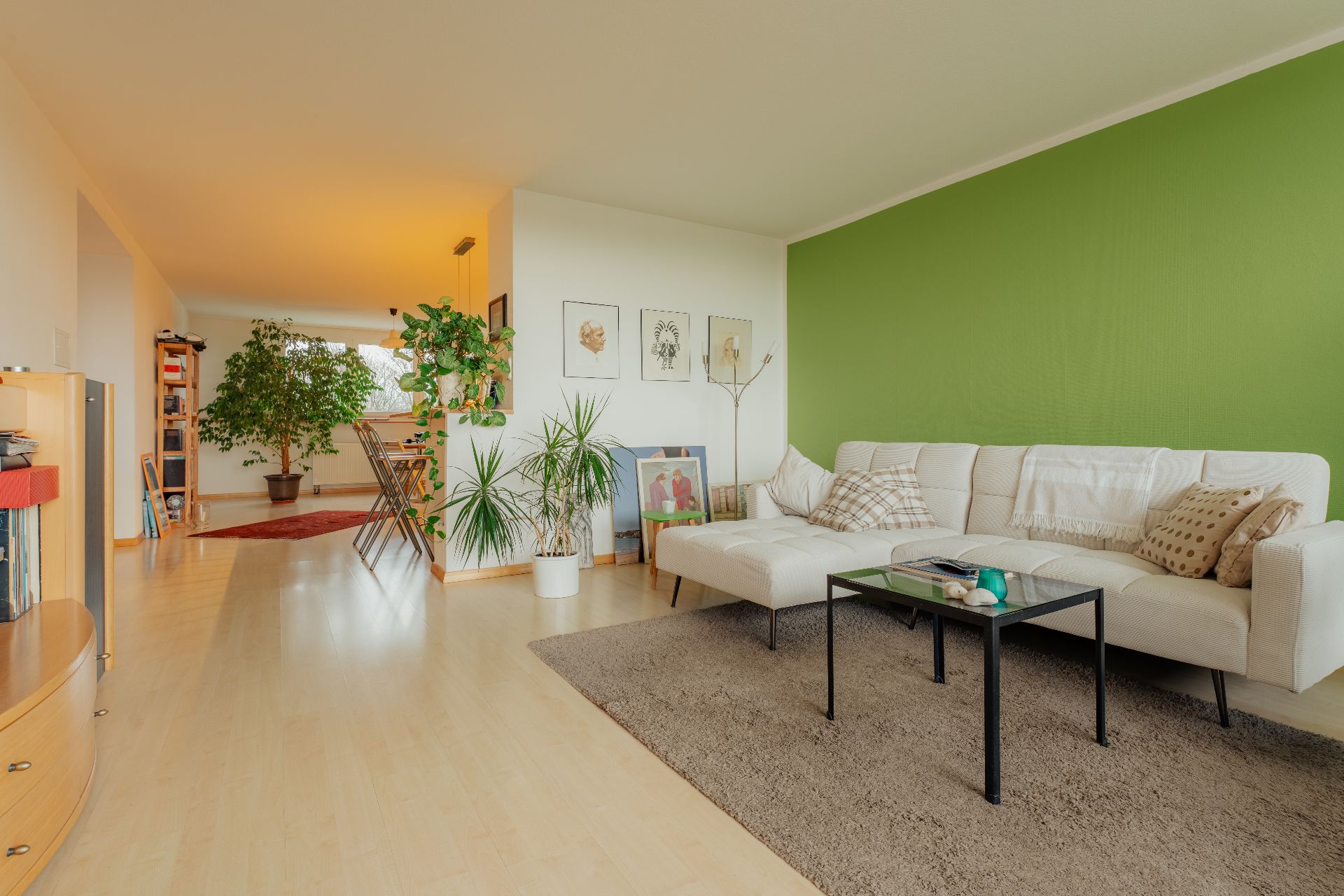 Modernes Wohnzimmer mit grüner Wand, weißem Sofa, Couchtisch und vielen Zimmerpflanzen.
