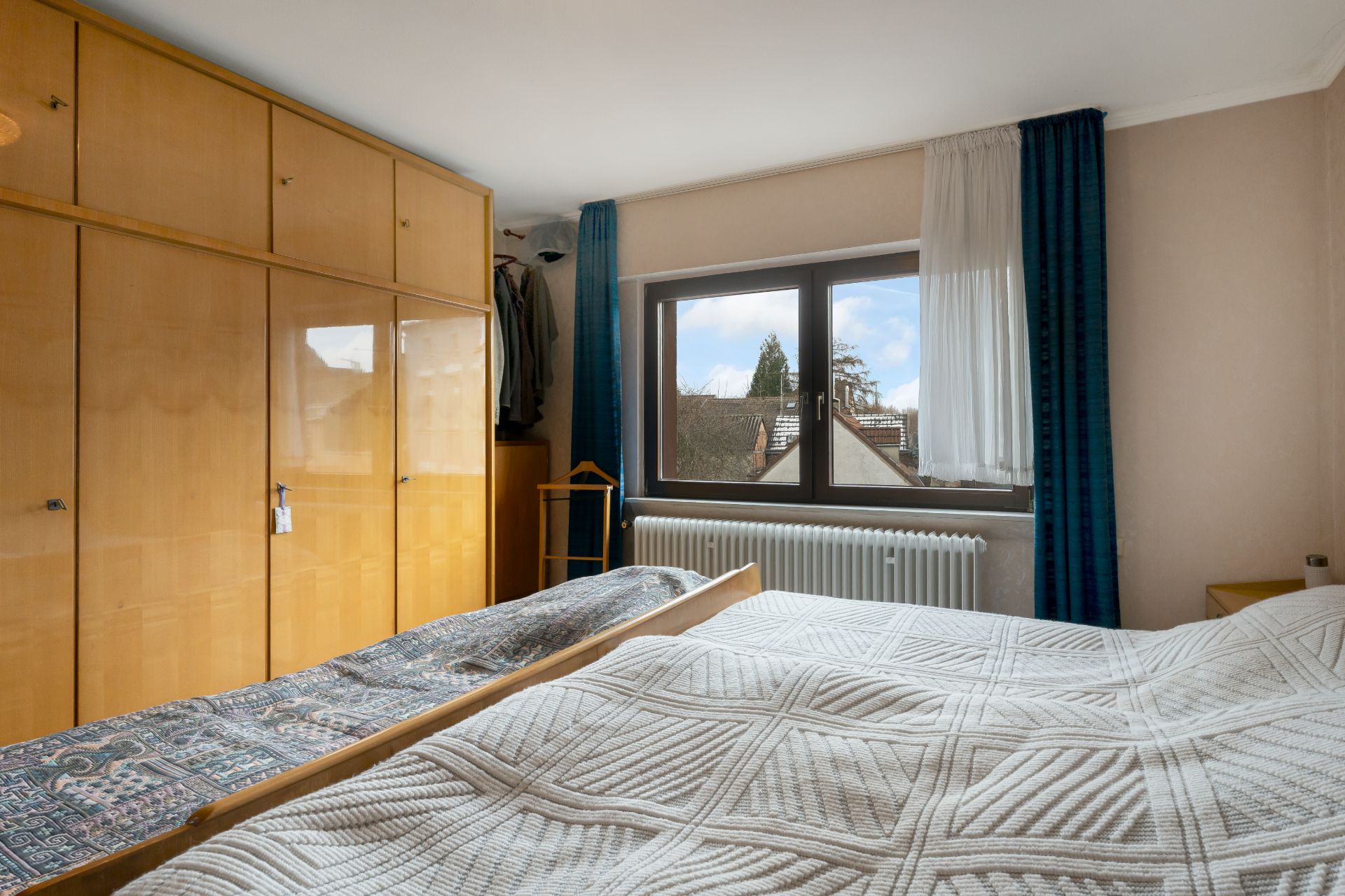 Schlafzimmer mit großem Kleiderschrank, Doppelbett und Fenster mit blauen Vorhängen.