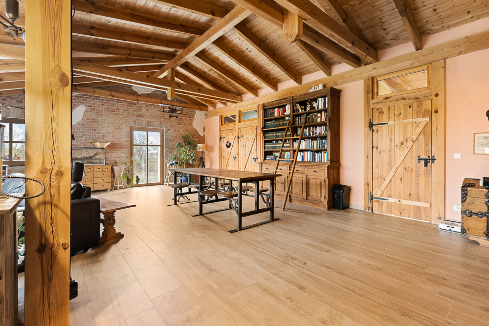 Großes Wohnzimmer mit Holzbalkendecke, Bücherregal, Holztüren, Tisch und Stühlen.
