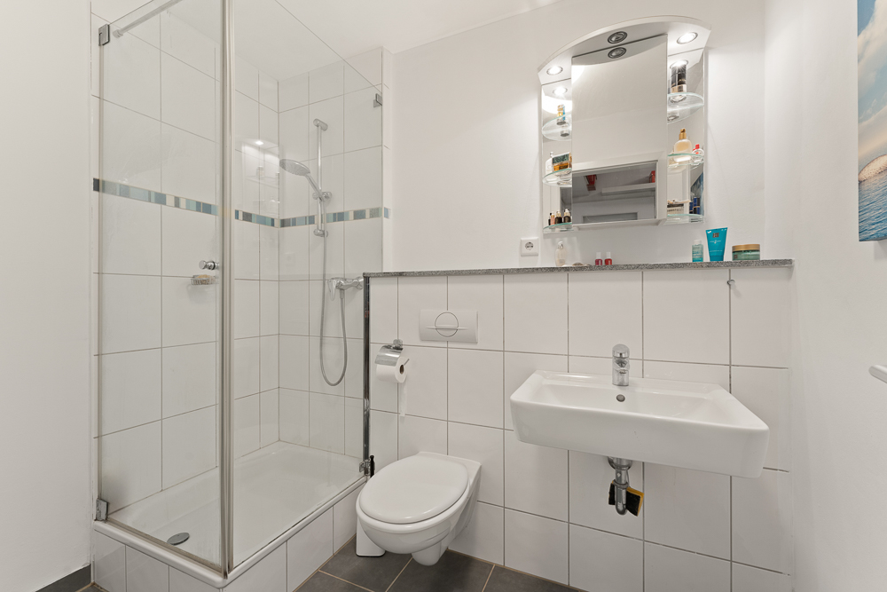Modernes Badezimmer mit Dusche, Toilette, Waschbecken und beleuchtetem Spiegel.