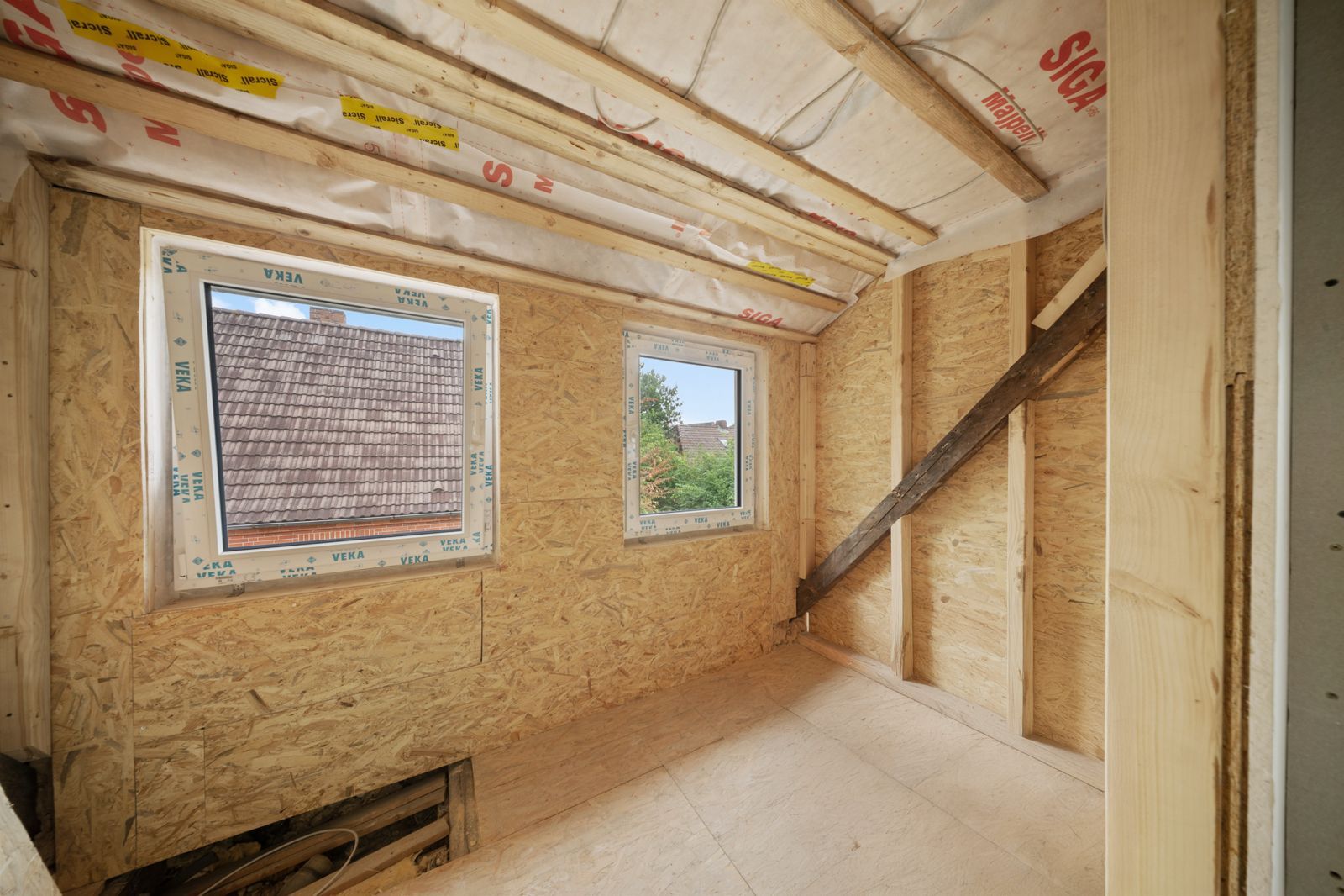 Kleiner Raum im Rohbau mit zwei Fenstern und sichtbarer Dämmung an Decke und Wänden.