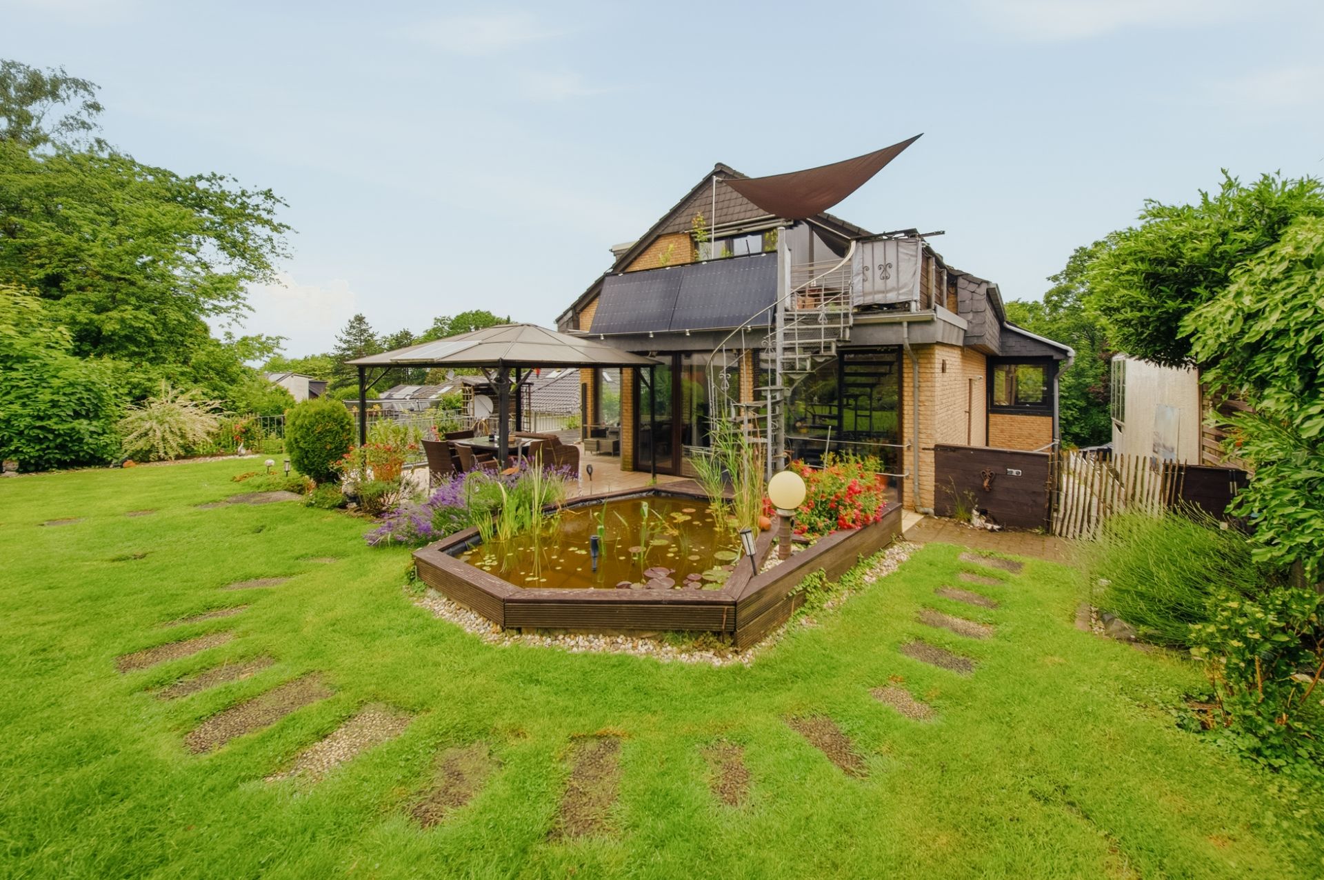 Modernes Haus mit Teich, Spiral-Außentreppe und Garten mit Sitzbereich.