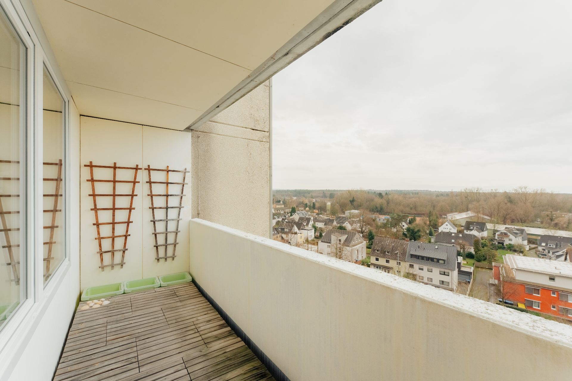 Balkon mit Holzlattenboden, Rankgittern an der Wand und Blick über Wohnhäuser.