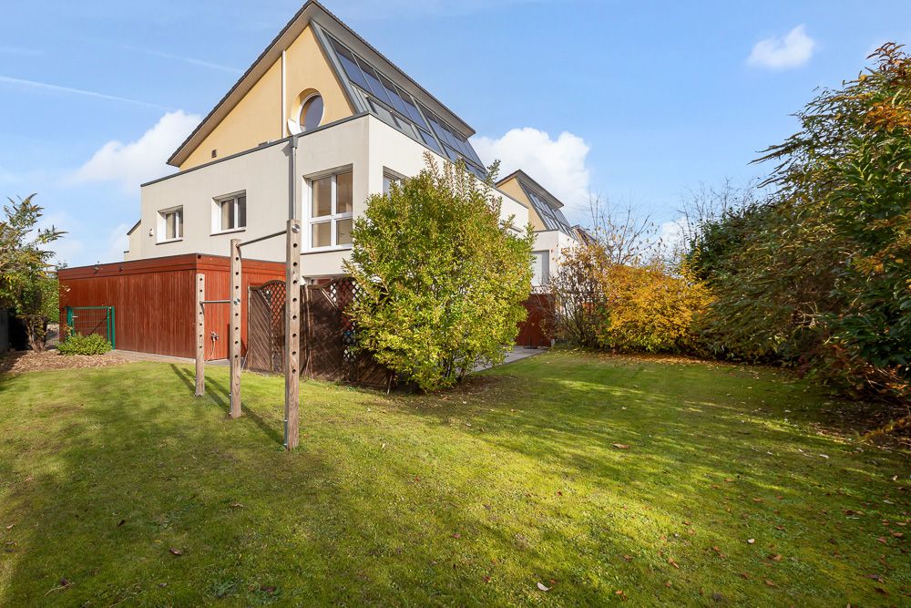 Modernes Wohnhaus mit großem Garten, Holzgarage und Solarpaneelen auf dem Dach.