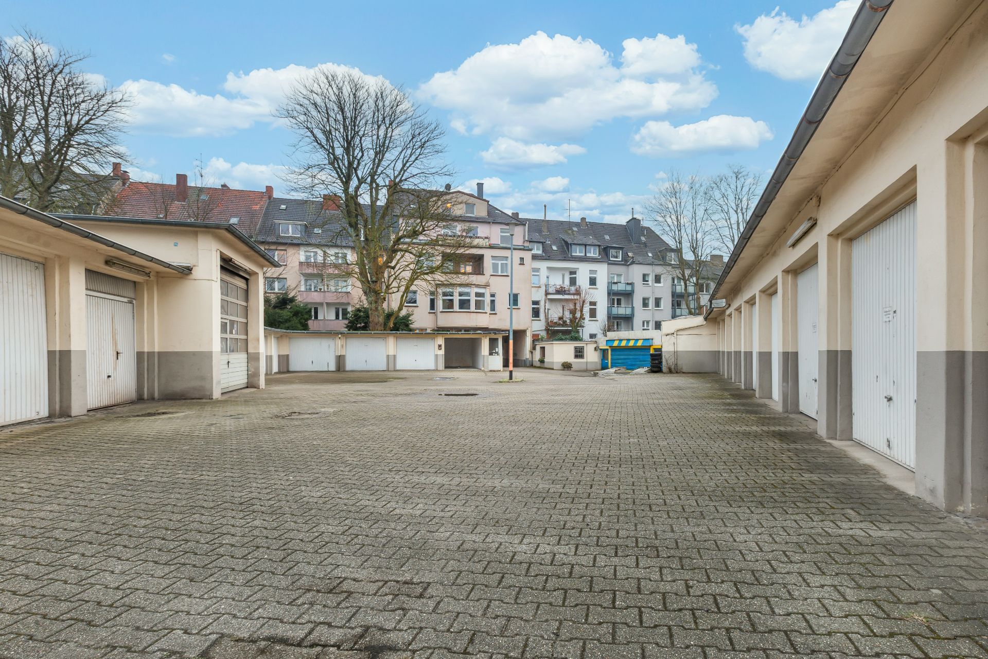 Gepflasterter Innenhof mit mehreren Garagentoren und Wohnhäusern im Hintergrund.
