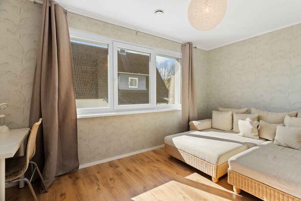 Helles Wohnzimmer mit großem Sofa, Holzfußboden, Schreibtisch und großem Fenster mit Vorhängen.