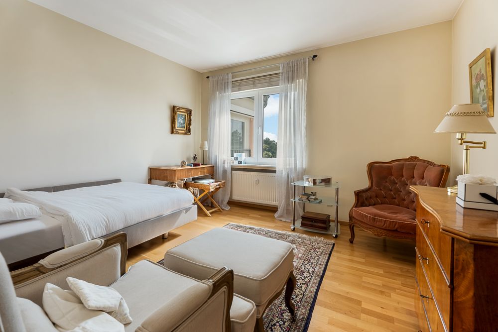 Helles Schlafzimmer mit Bett, Sessel, Schreibtisch, Teppich und Fenster.