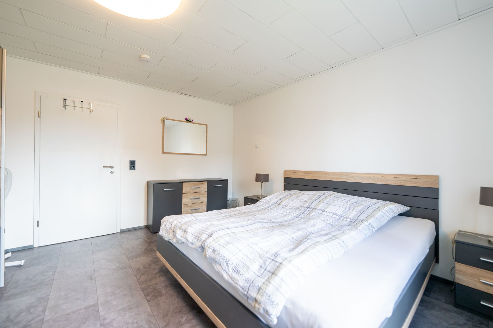 Helles Schlafzimmer mit Doppelbett, Nachttischen, Kommode und Wandspiegel.