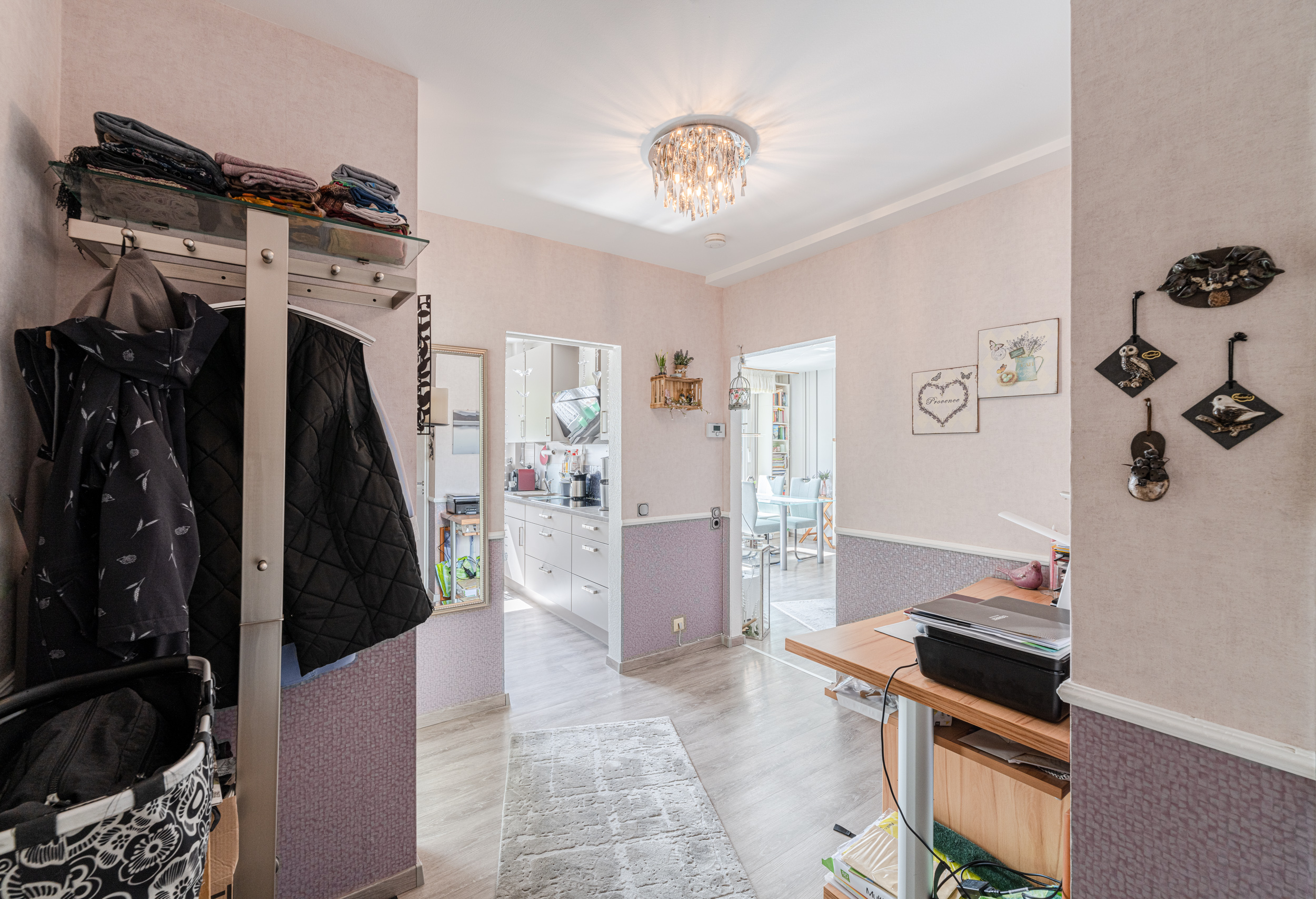 Flur mit Garderobe, Schreibtisch, hellen Wänden und Blick in Küche und Esszimmer.