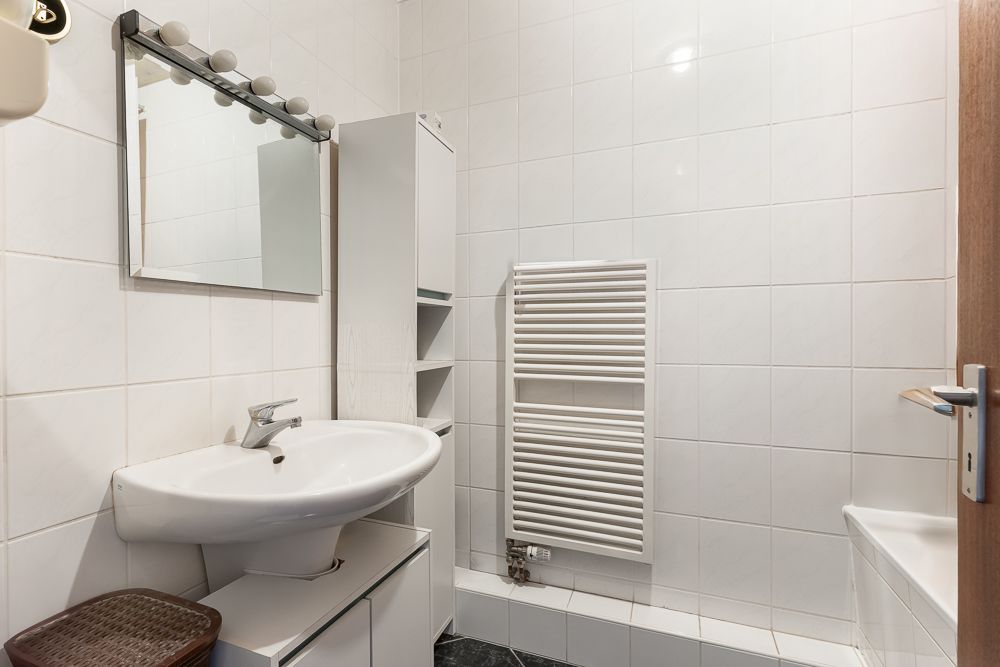 Helles Badezimmer mit Waschbecken, Spiegel, Handtuchheizkörper und weißen Fliesen.