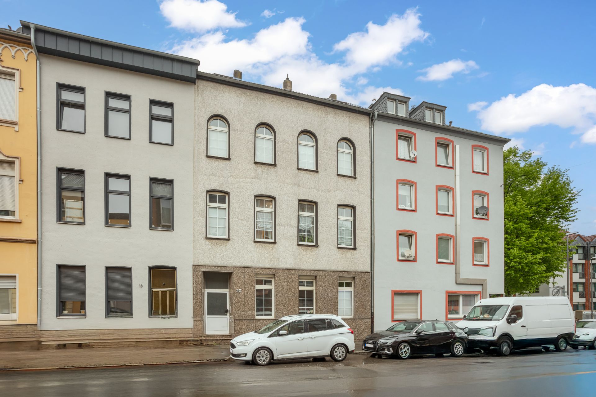 Reihenhausfassaden mit geparkten Autos an einer Straße bei Tageslicht.