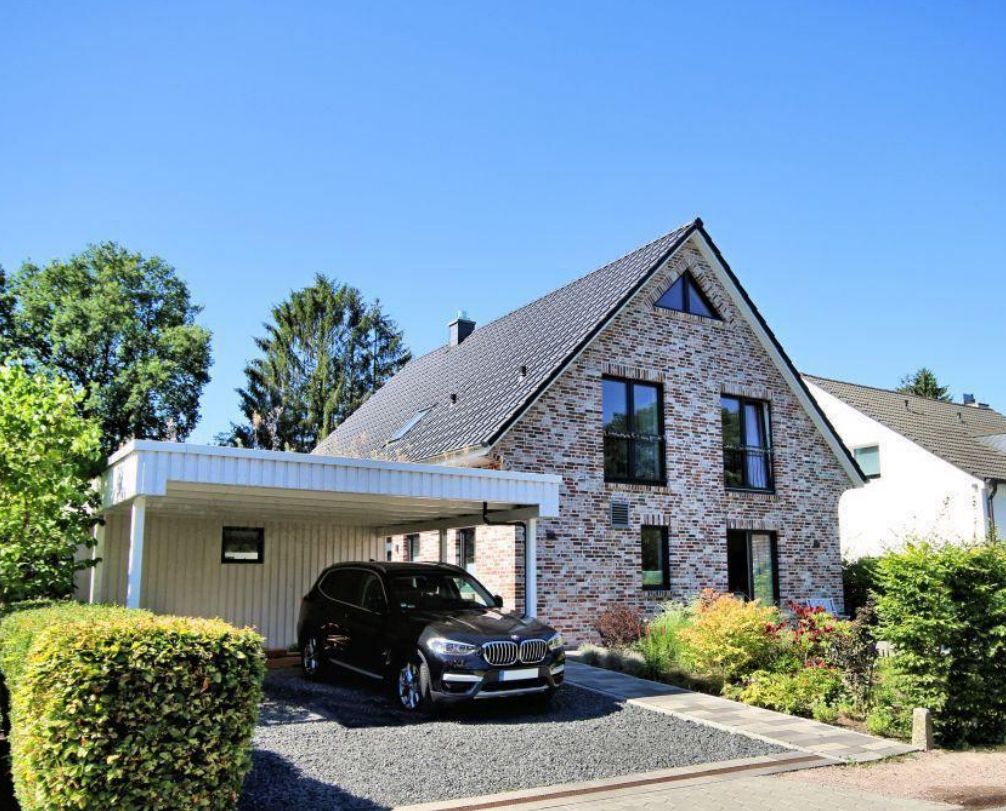 Modernes Einfamilienhaus aus Klinker mit Carport und schwarzem Auto, umgeben von Garten.