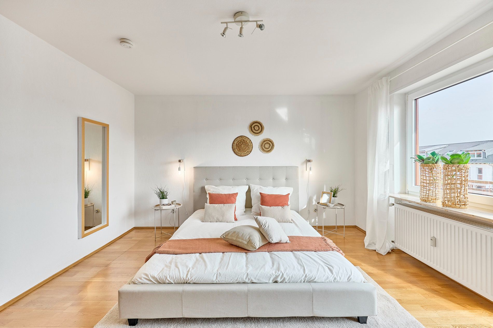 Helles Schlafzimmer mit Doppelbett, Holzboden, großem Fenster und Dekoration an der Wand.