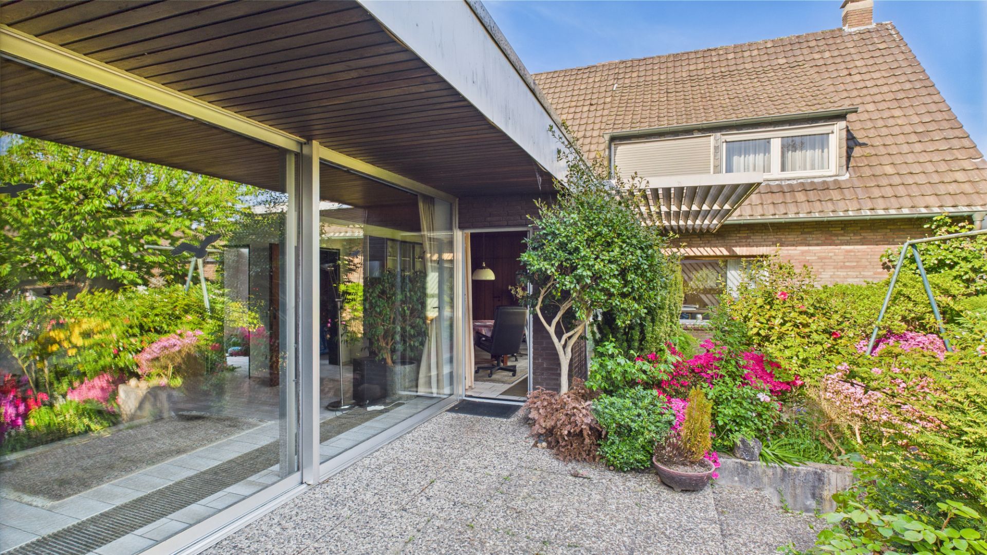 Gepflegter Garten mit bunten Blumen, Terrasse und Blick auf ein Wohnhaus mit großen Fenstern.