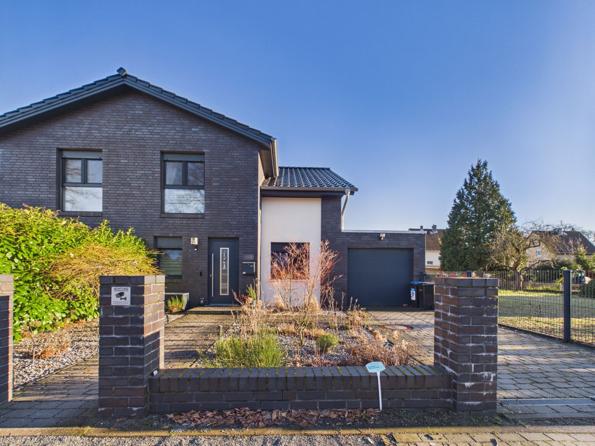 Modernes Einfamilienhaus mit dunkler Fassade, Vorgarten, Einfahrt und Garage.