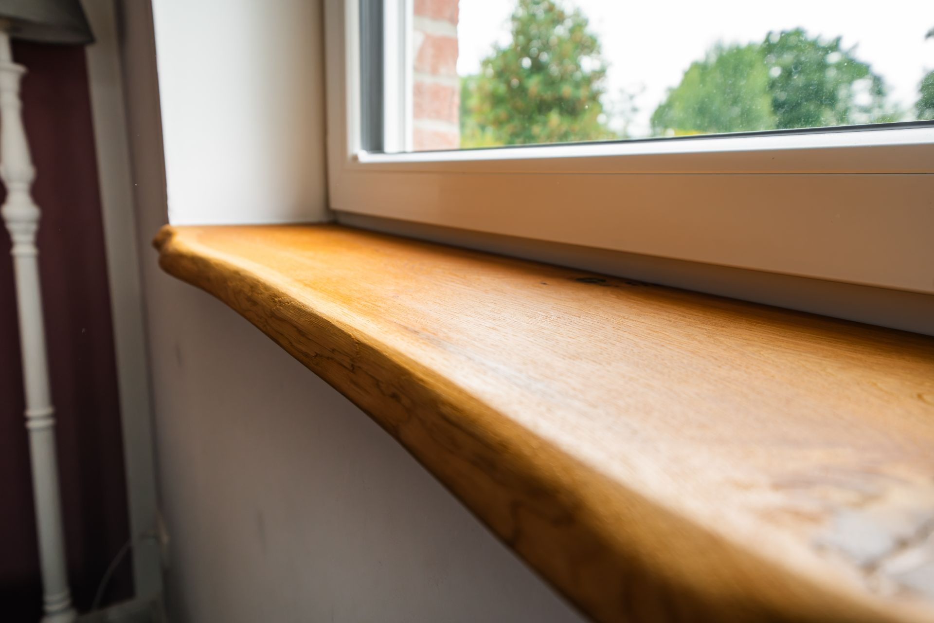 Nahaufnahme einer hölzernen Fensterbank an einem Fenster mit Blick ins Grüne.