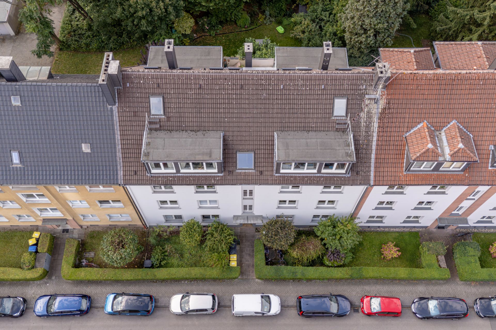 Draufsicht auf Wohnhäuser, Vorgärten und parkende Autos am Straßenrand.