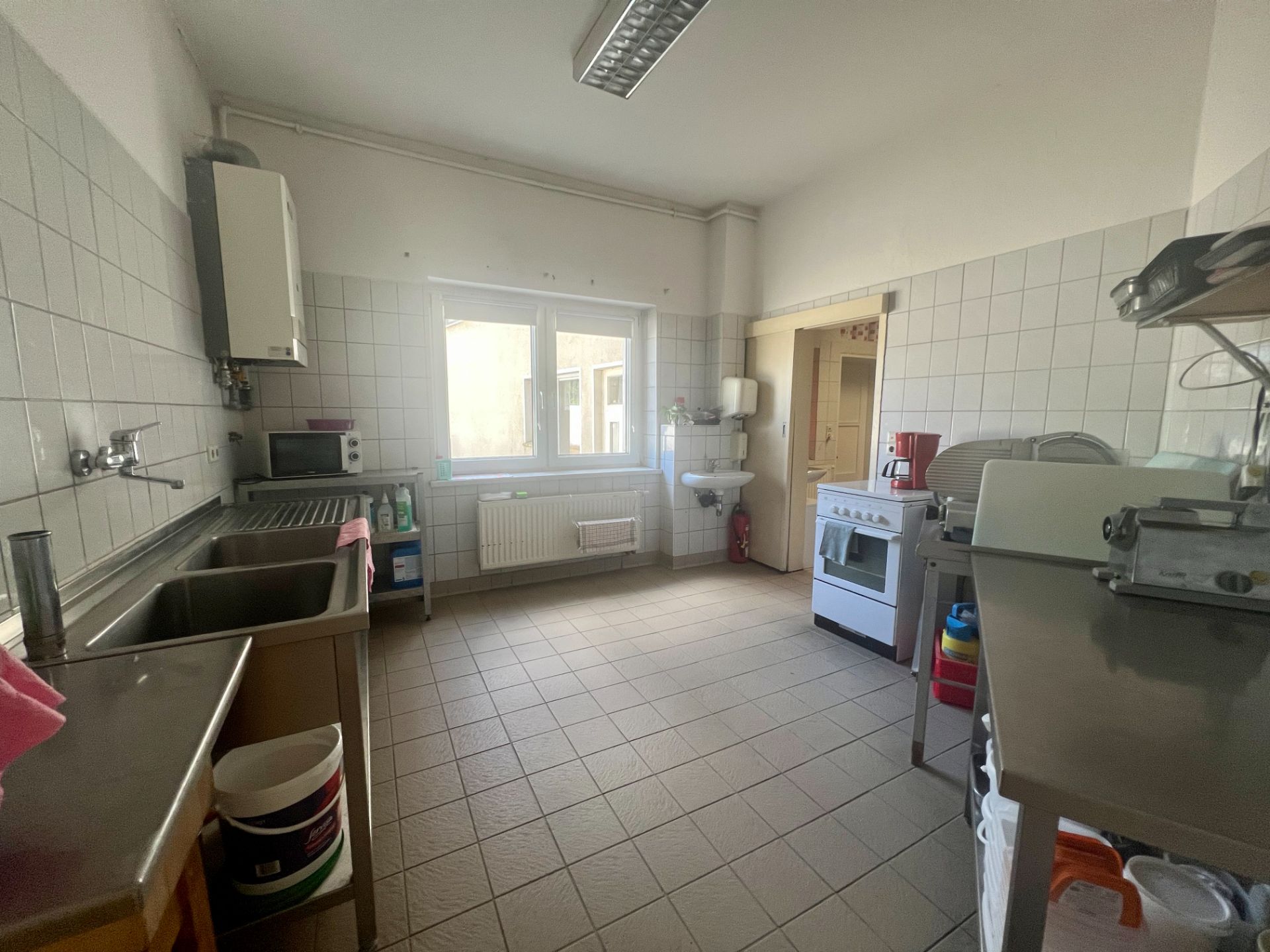 Helle Küche mit Fenster, Spüle, Herd, Waschbecken und Haushaltsgeräten.