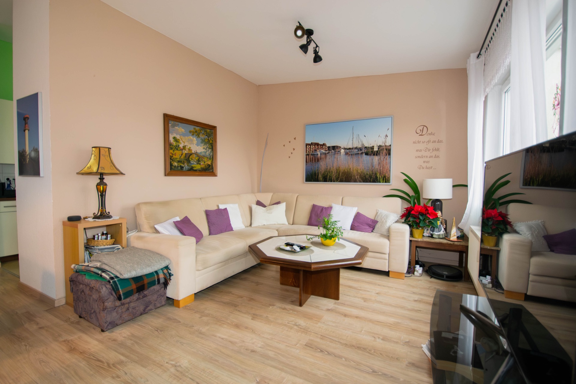 Gemütliches Wohnzimmer mit Ecksofa, Couchtisch, Pflanzen und Bildern an der Wand.